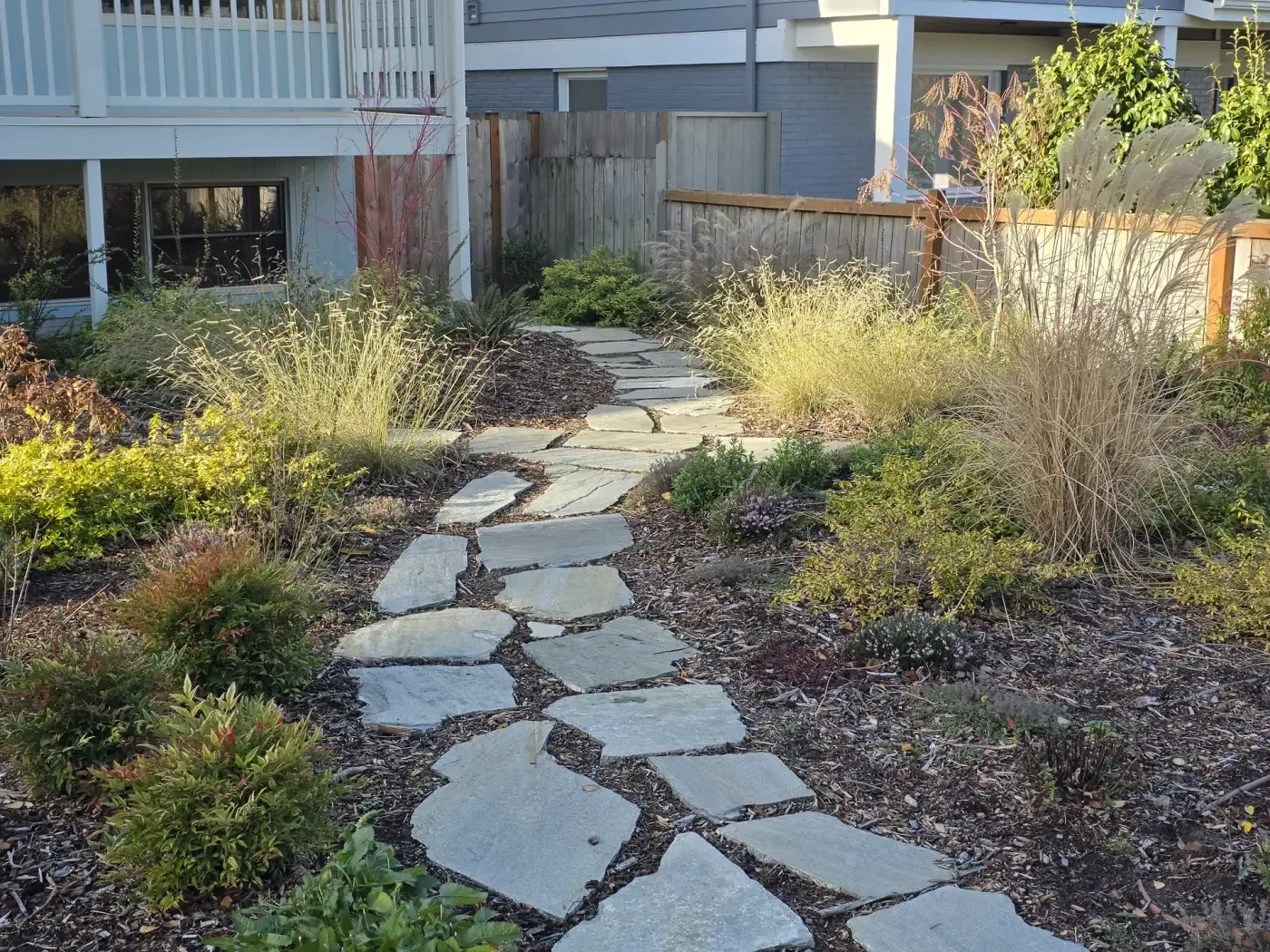 Wide view of stone path curving through grasses toward fence