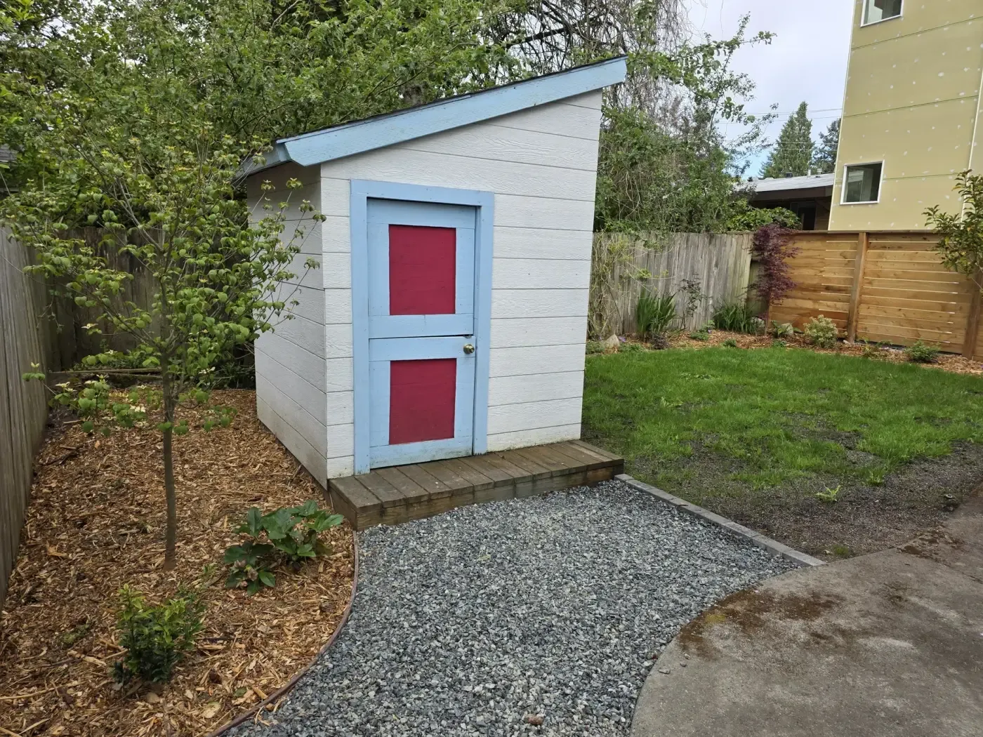 Crushed rock walkway curving to shed, mulched bed and fence