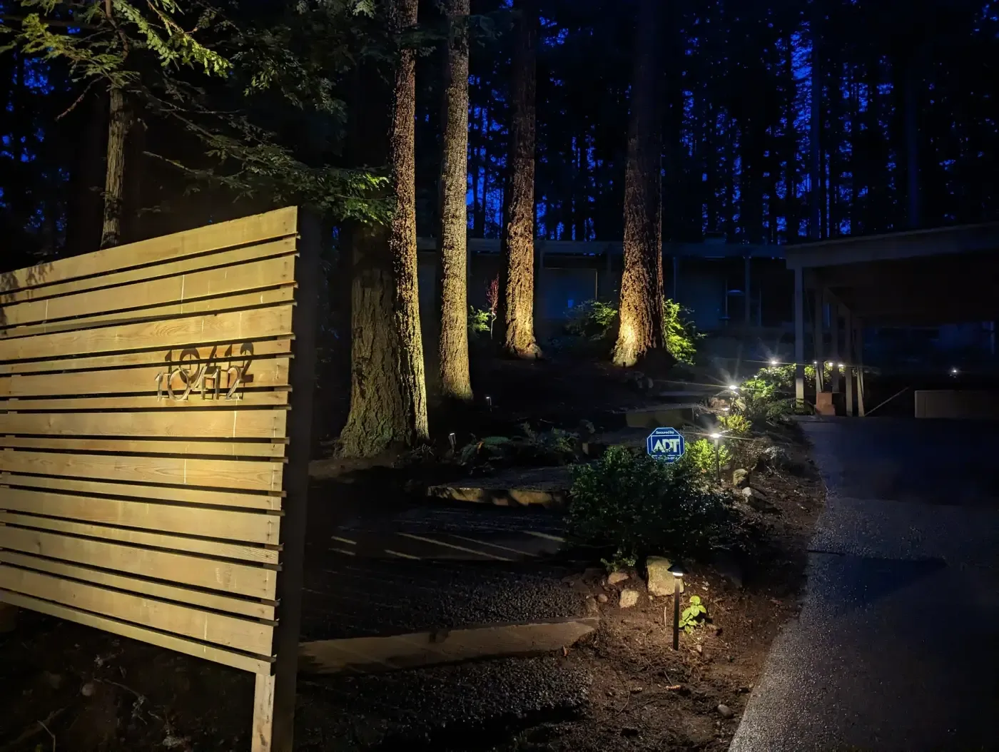 Evening shot of lit fence panel, tree uplights and bed fixtures