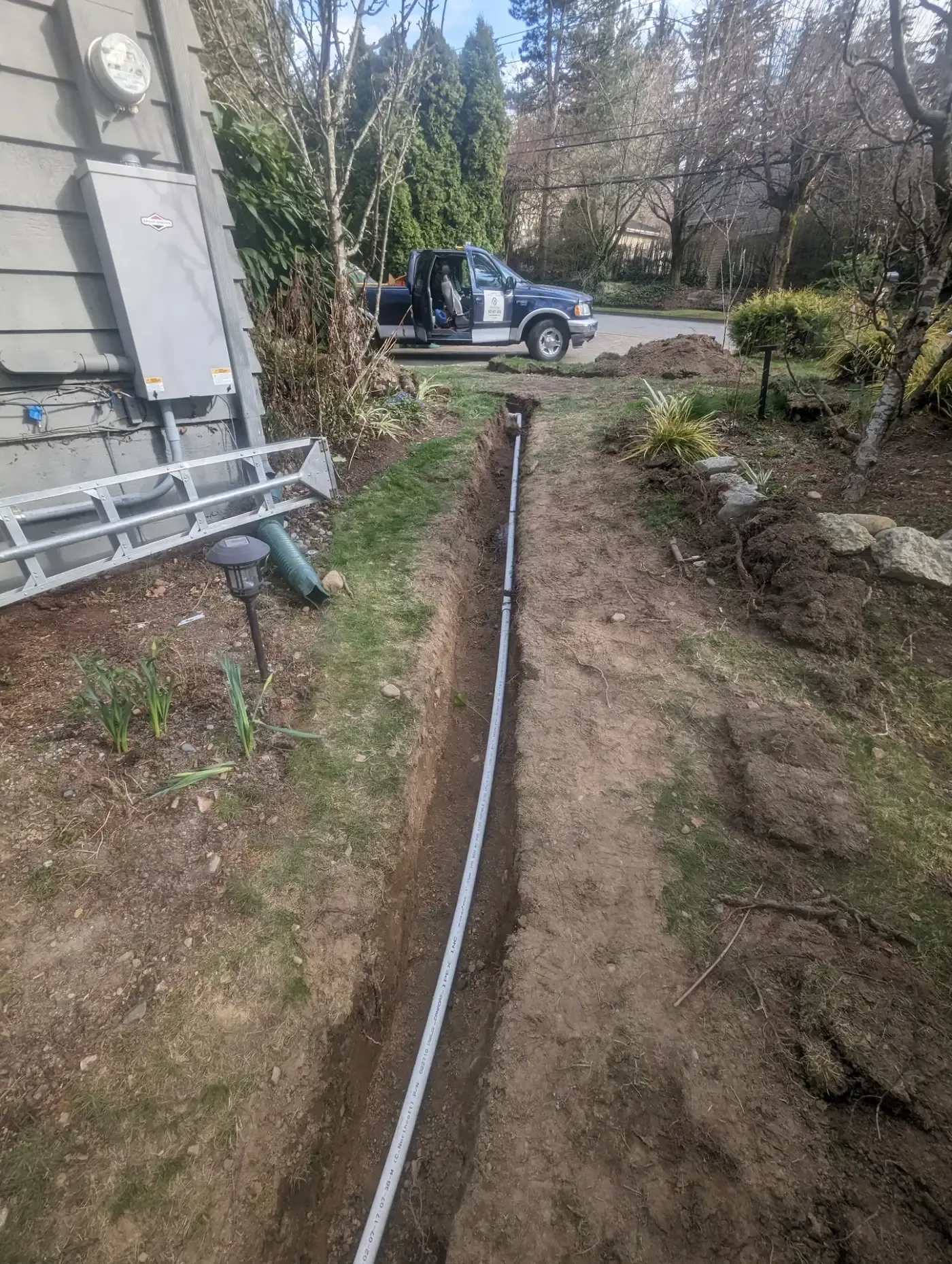 Long open trench with white pipe running along side yard