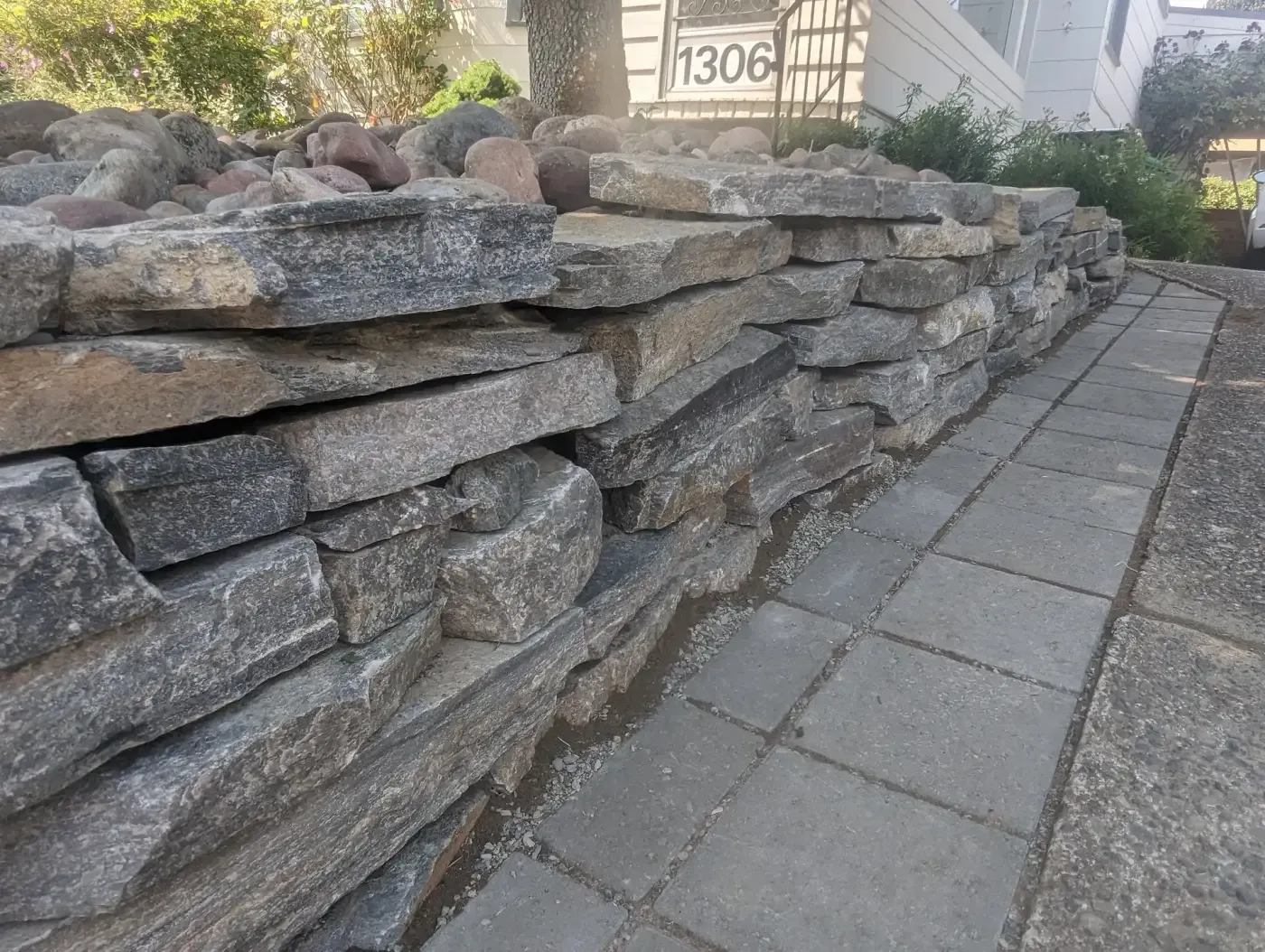 Close view along stacked grey stone wall next to paver walkway