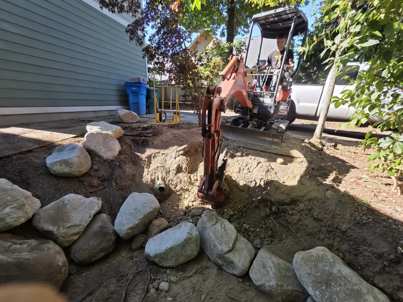 Compact excavator trenching next to granite boulder wall