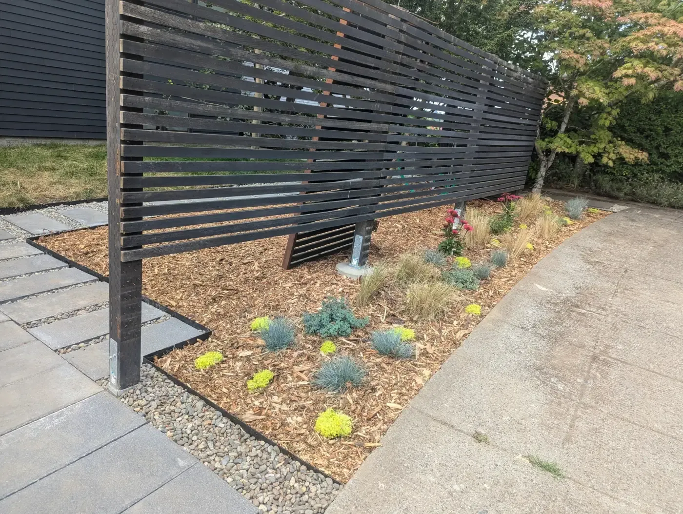 Freestanding black slat panels on posts above mulch bed