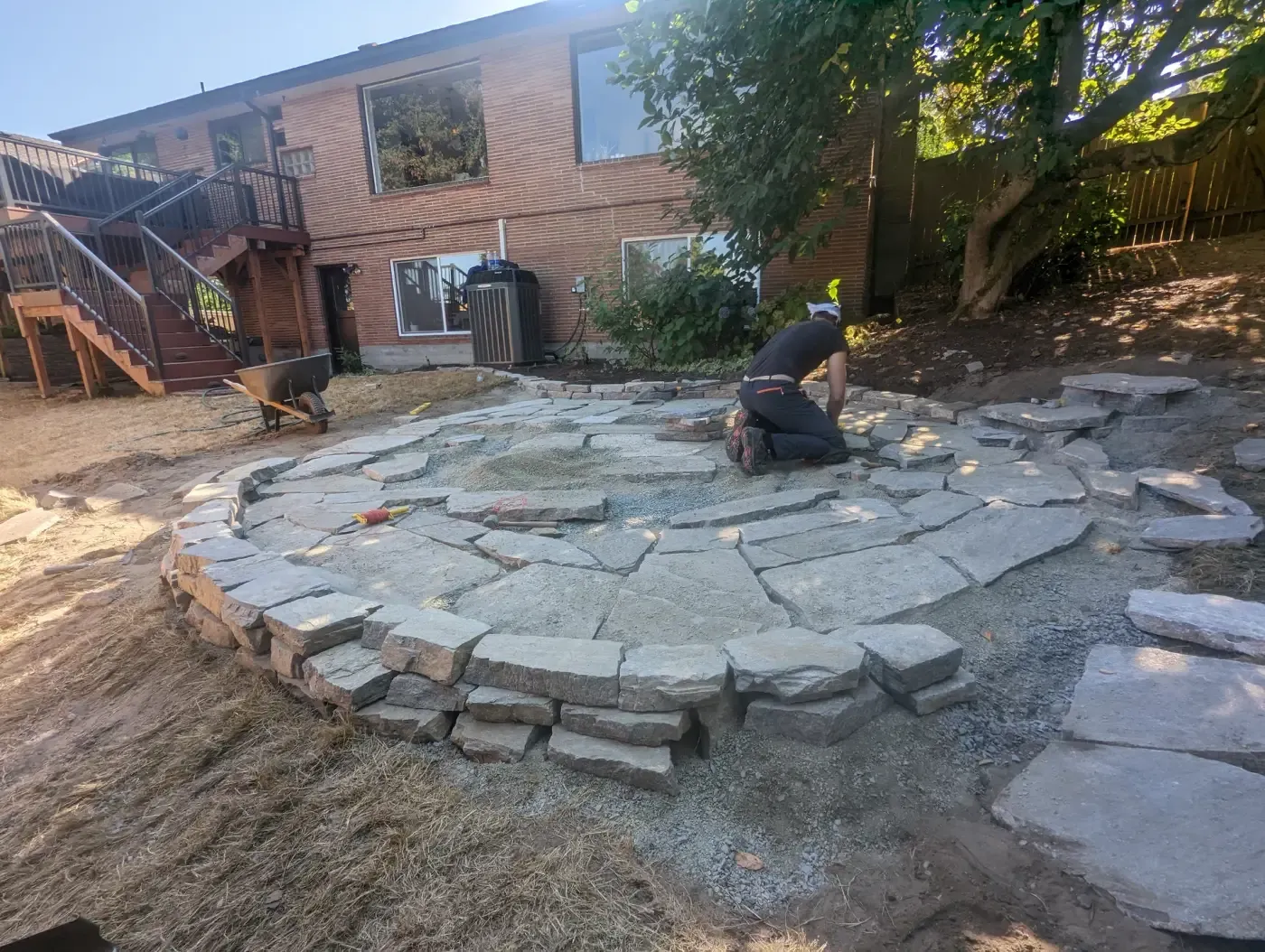 Circular stone patio nearing completion behind brick house
