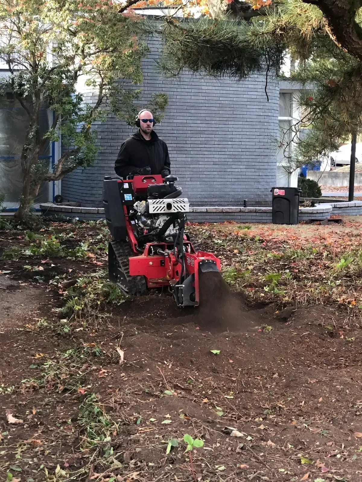 Crew member working red walk-behind grinder in bare soil bed