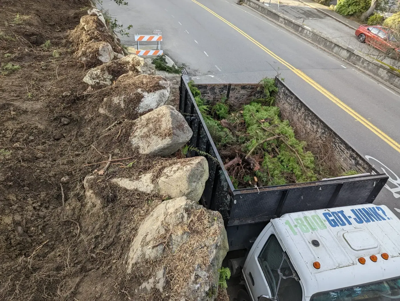 Hillside cleared of brush, boulders exposed, debris truck at roadside