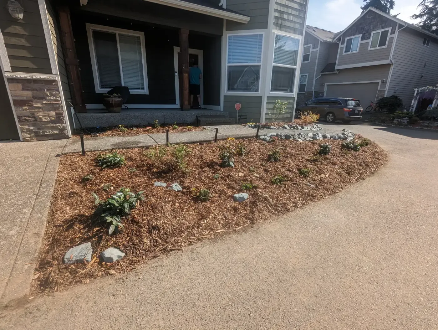 Curved bark bed with young shrubs, path light stakes, white rocks