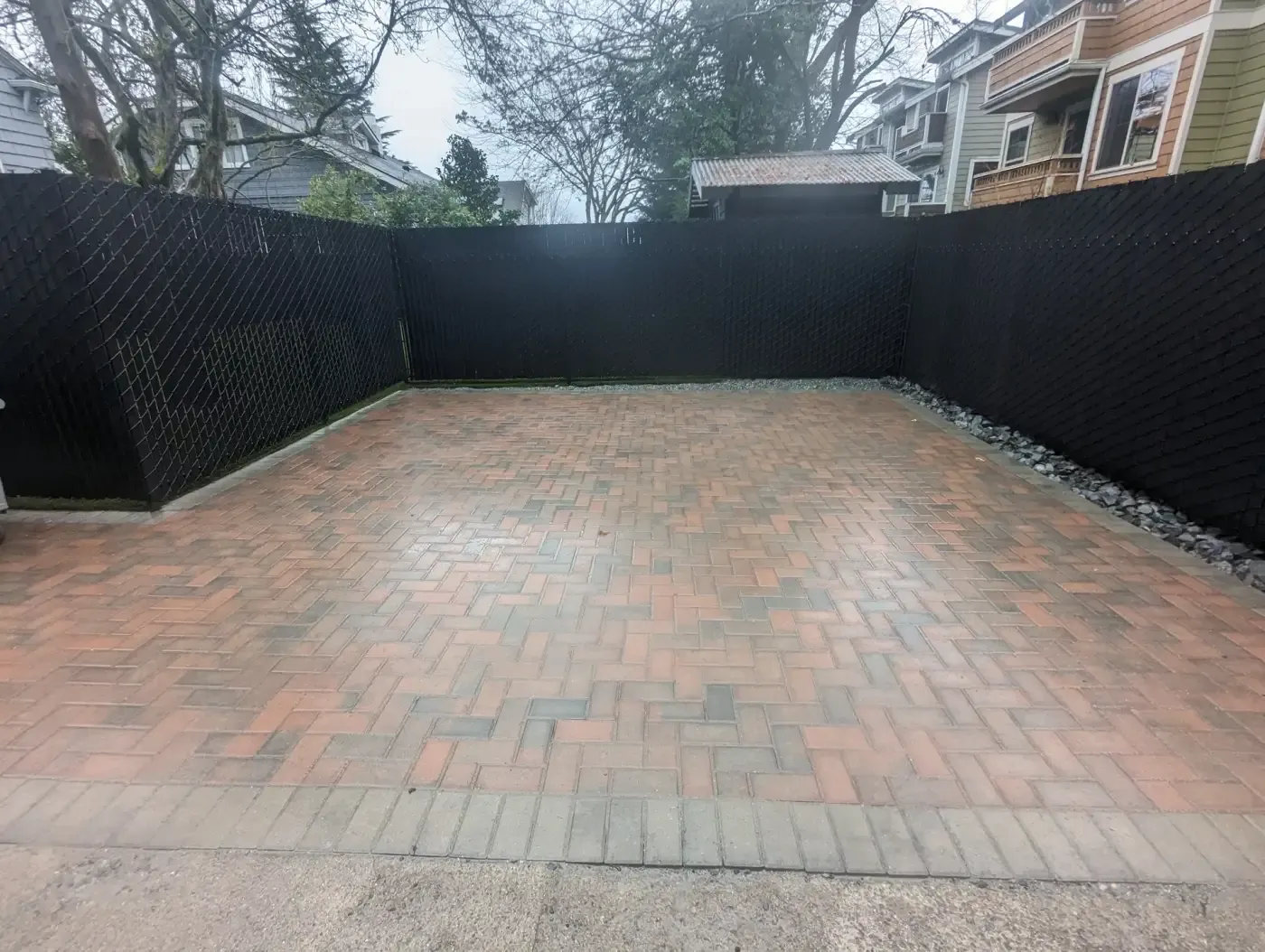 Large brick paver pad enclosed by black slatted fence