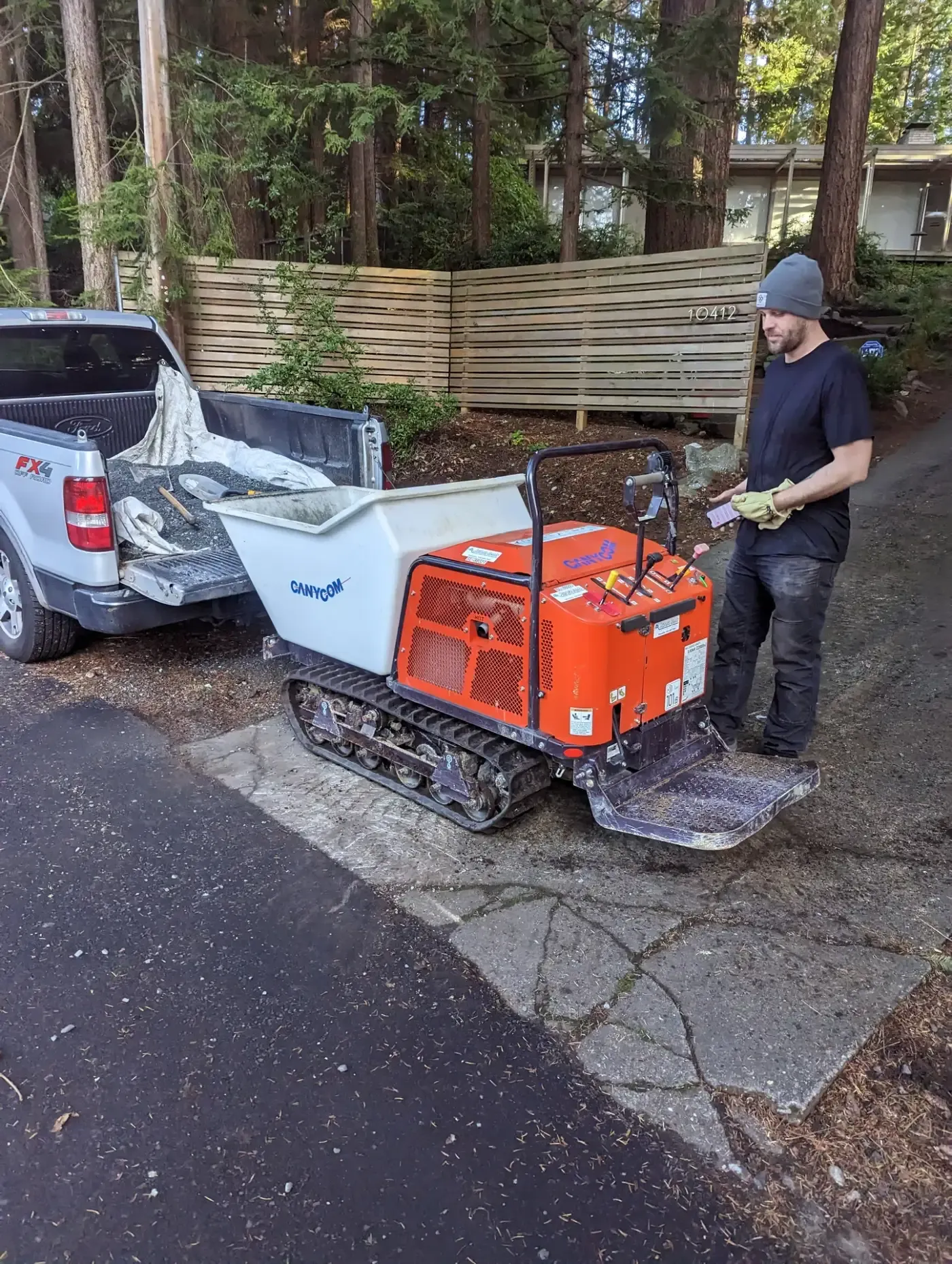 Crew member with tracked material dumper beside pickup in driveway