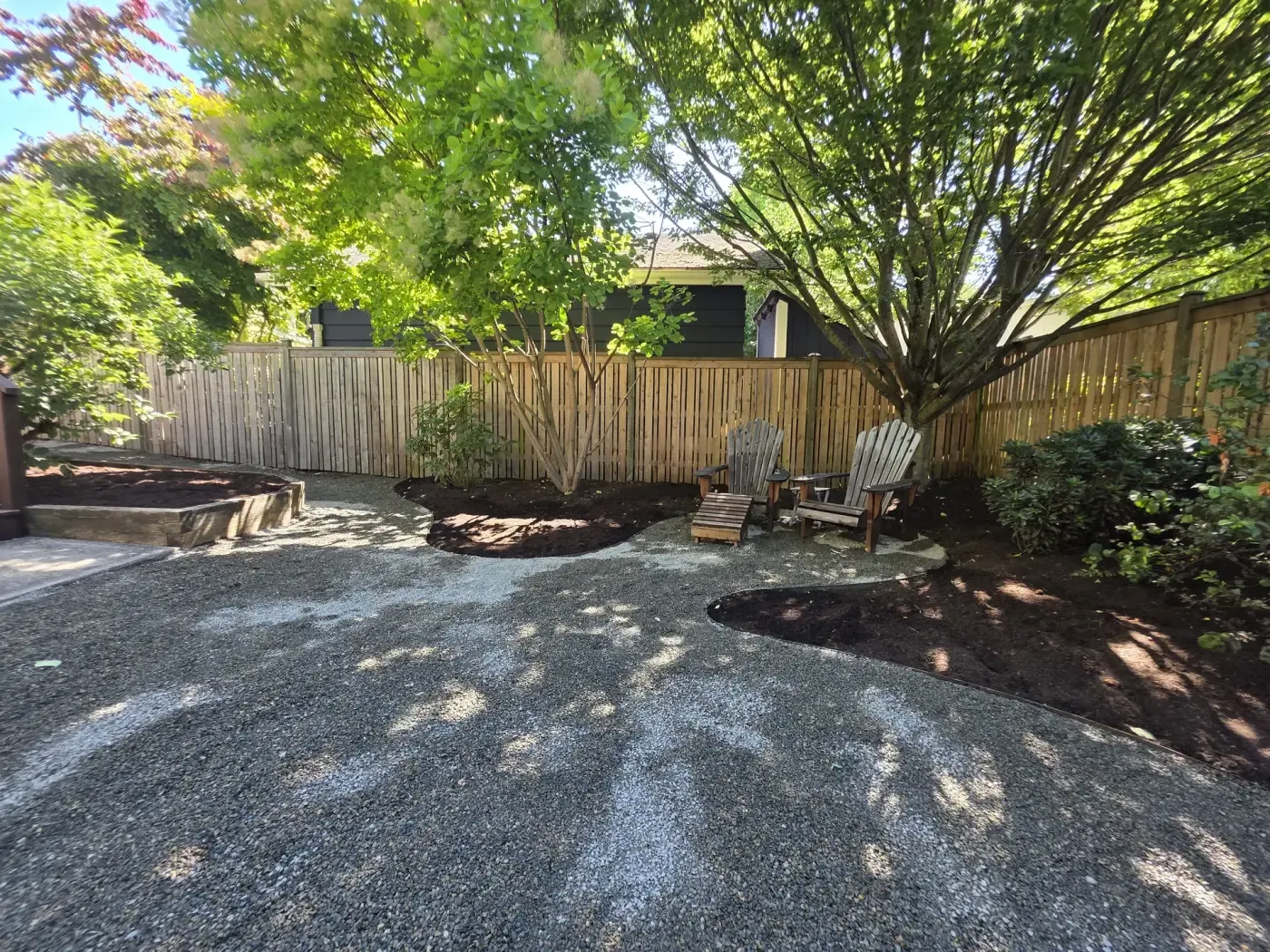 Wide gravel courtyard, bark beds, cedar fence, shade trees