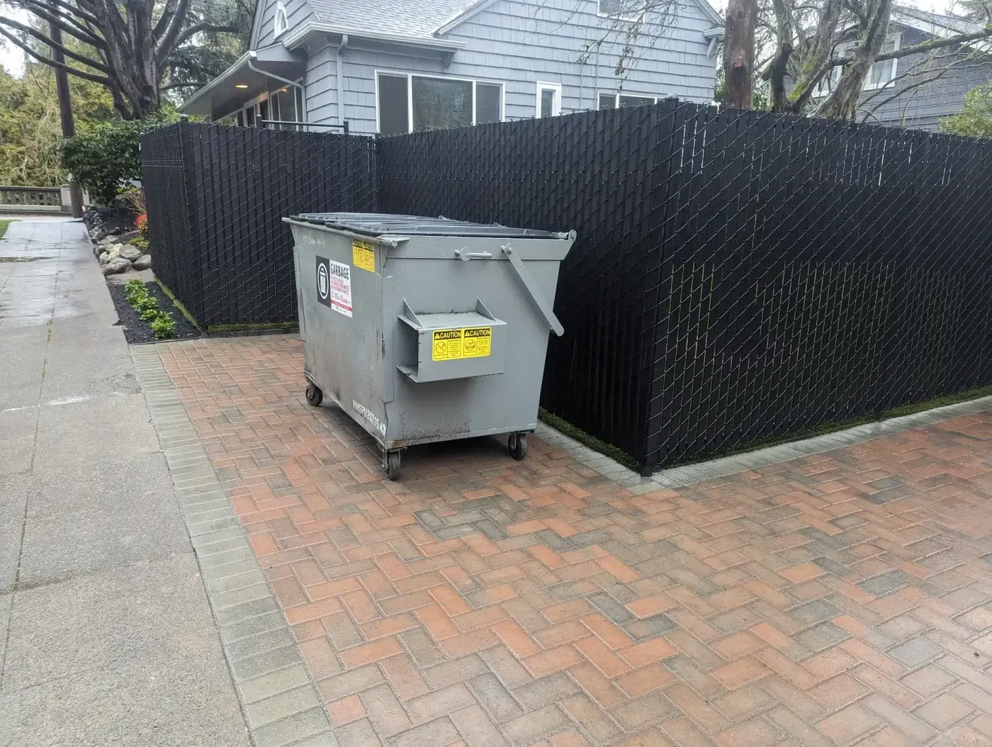 Privacy-slat chain-link screen around paved trash enclosure