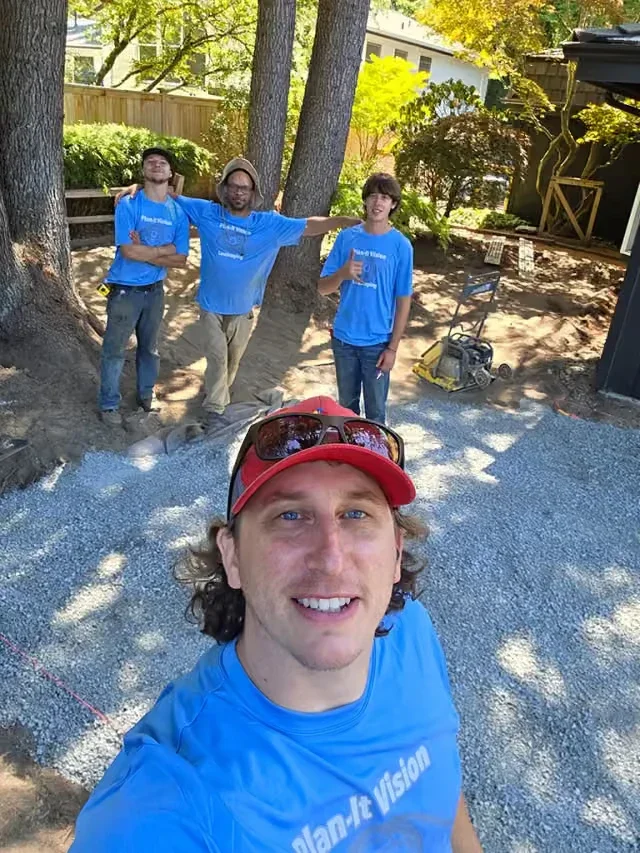 Trevor Kokenge with three of the crew in Plan-It Vision shirts on a job site, compacted gravel base and a plate compactor behind them