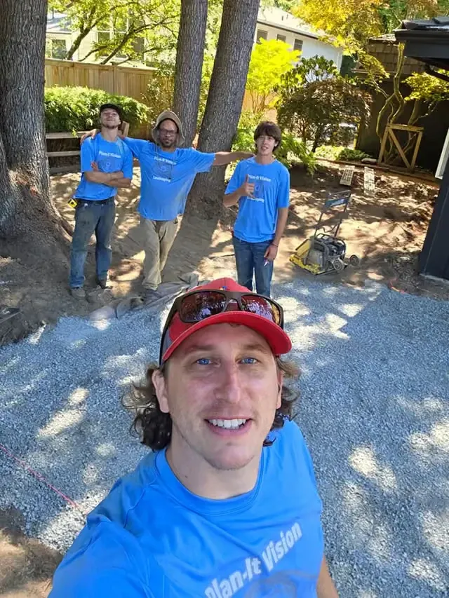 Trevor Kokenge with three of the crew in Plan-It Vision shirts on a job site, compacted gravel base and a plate compactor behind them