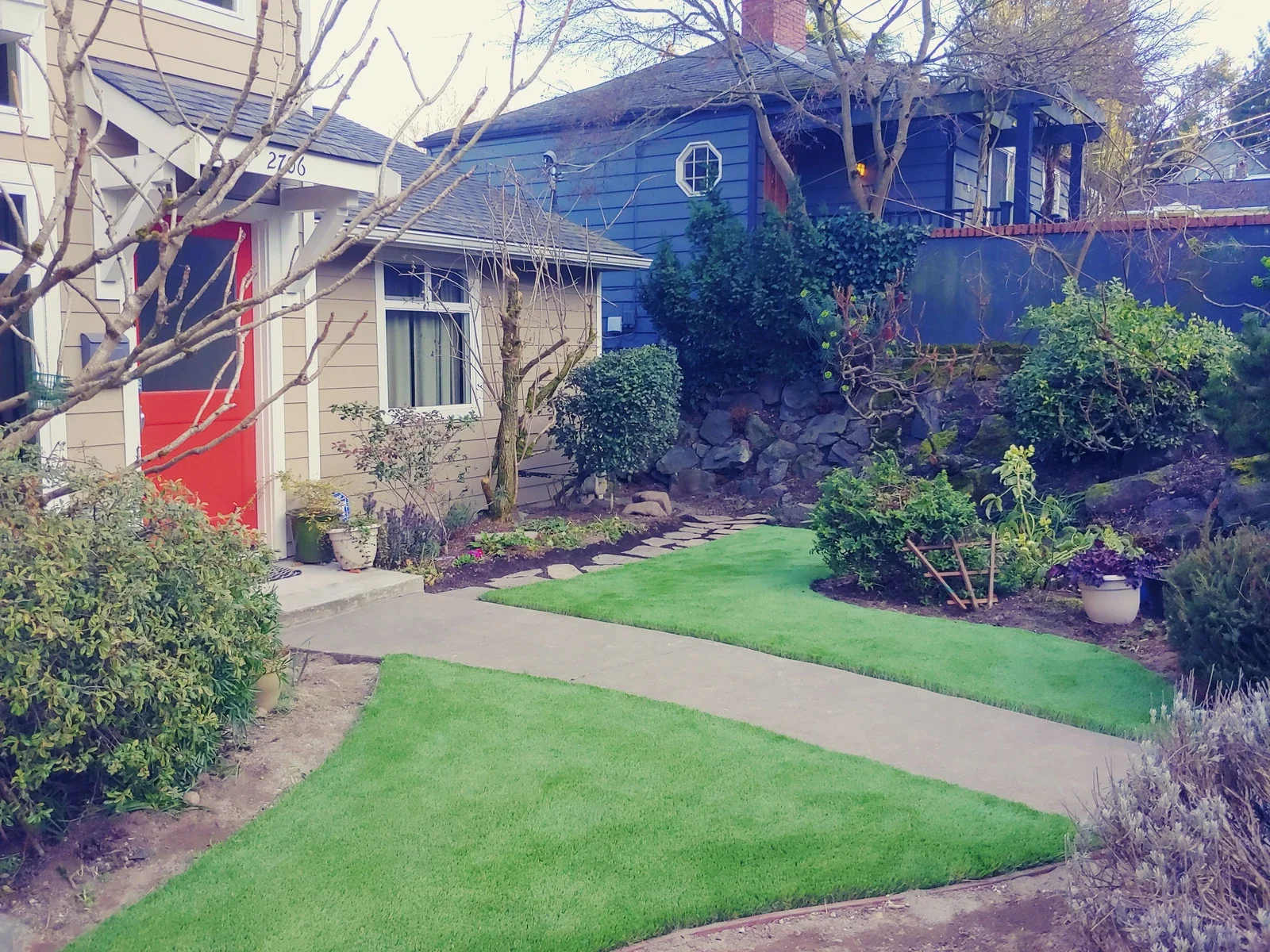 Artificial turf lawn curving along a concrete walk to a house with a red front door