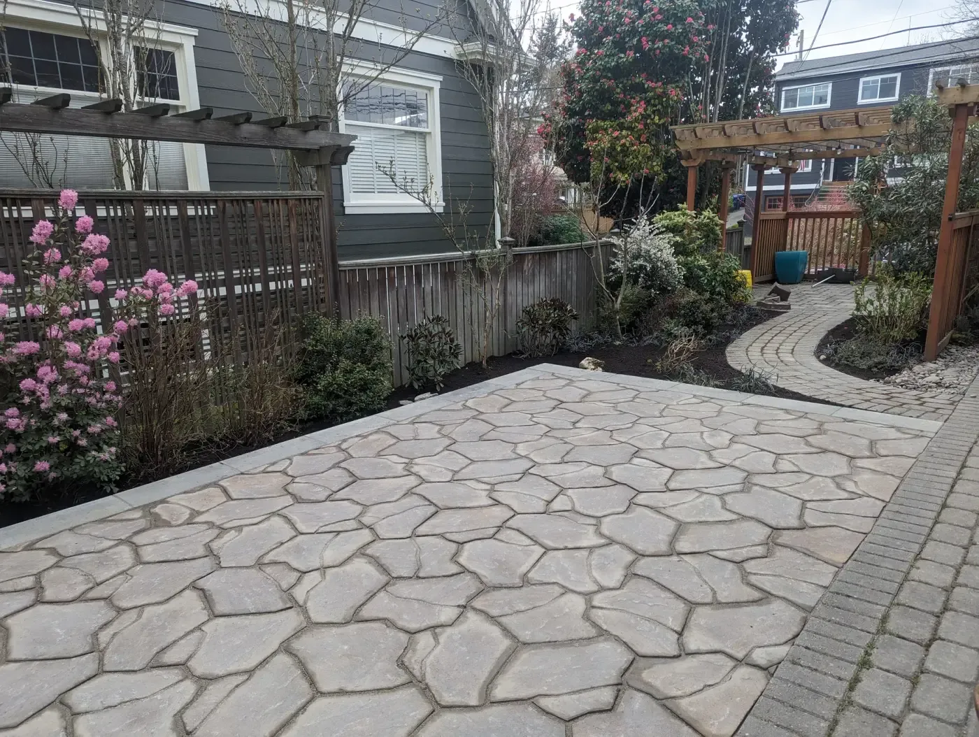 Finished stone-look patio with pink rhododendron and arbor