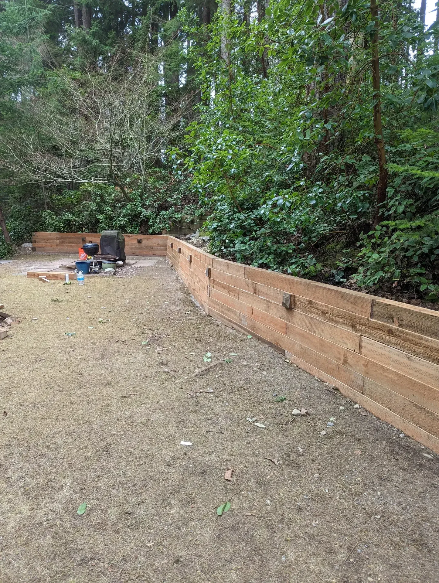 New stacked timber retaining wall curving along a graded yard in forest