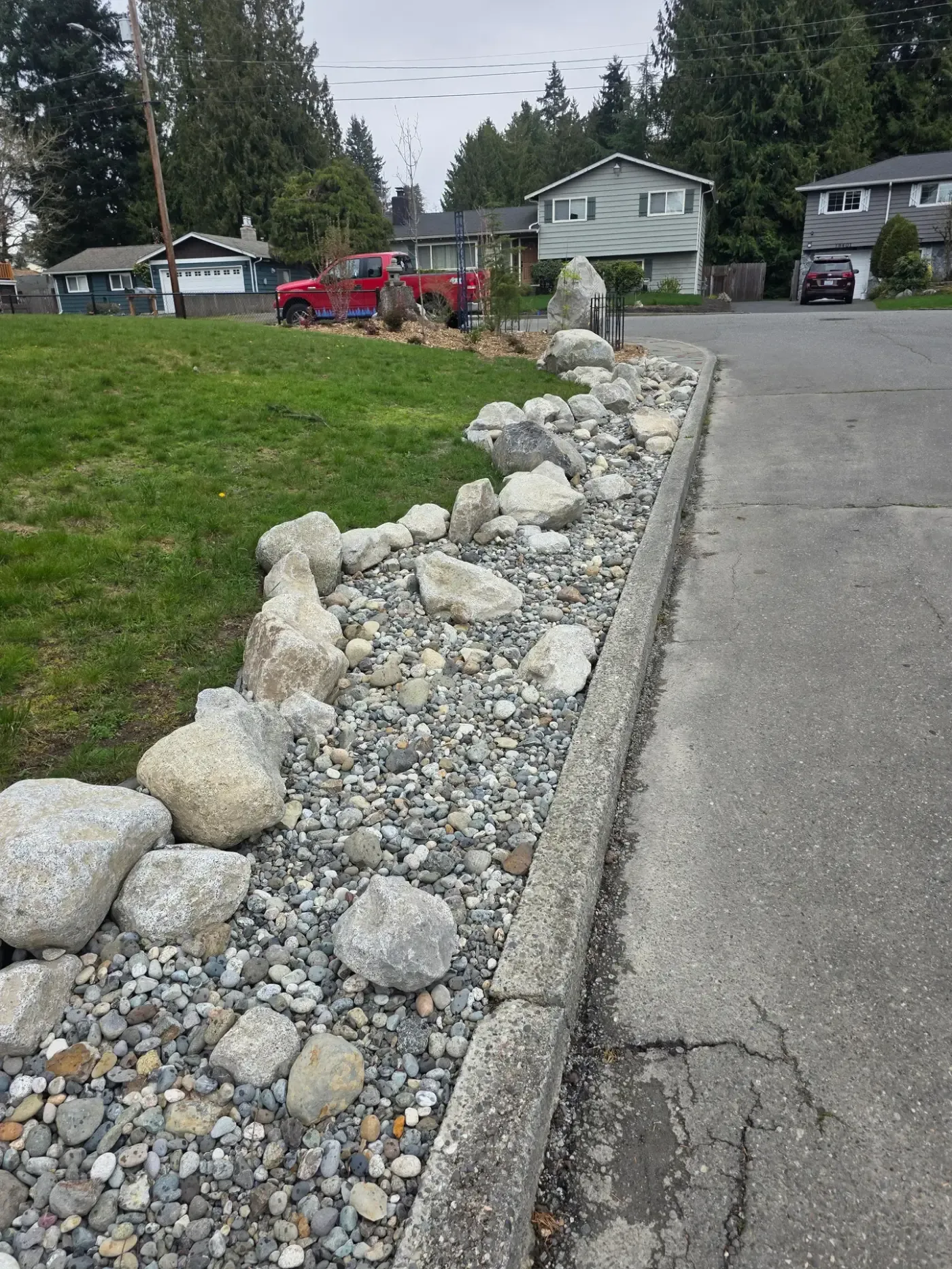 Granite boulders set in a river rock strip between a lawn and the street curb