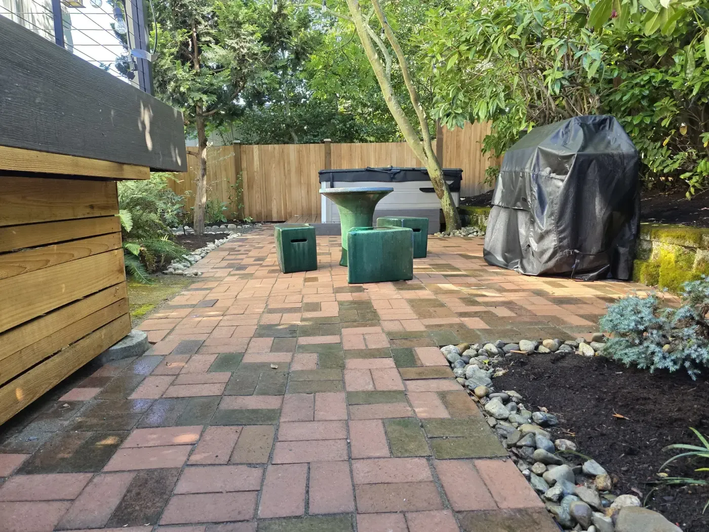 Multicolor brick pavers, hot tub, grill, river rock border