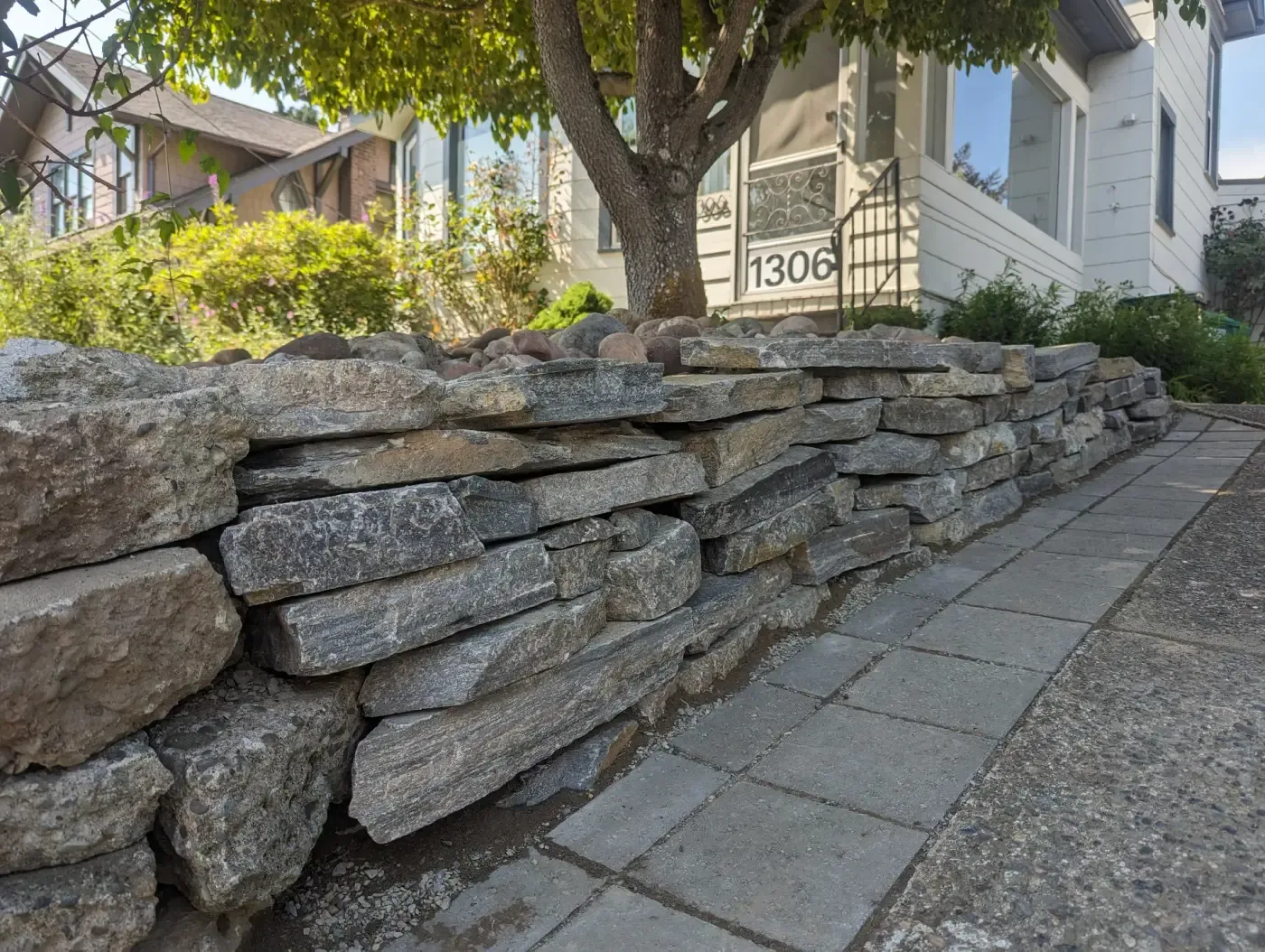 Stone retaining wall fronting house with grey paver walkway alongside