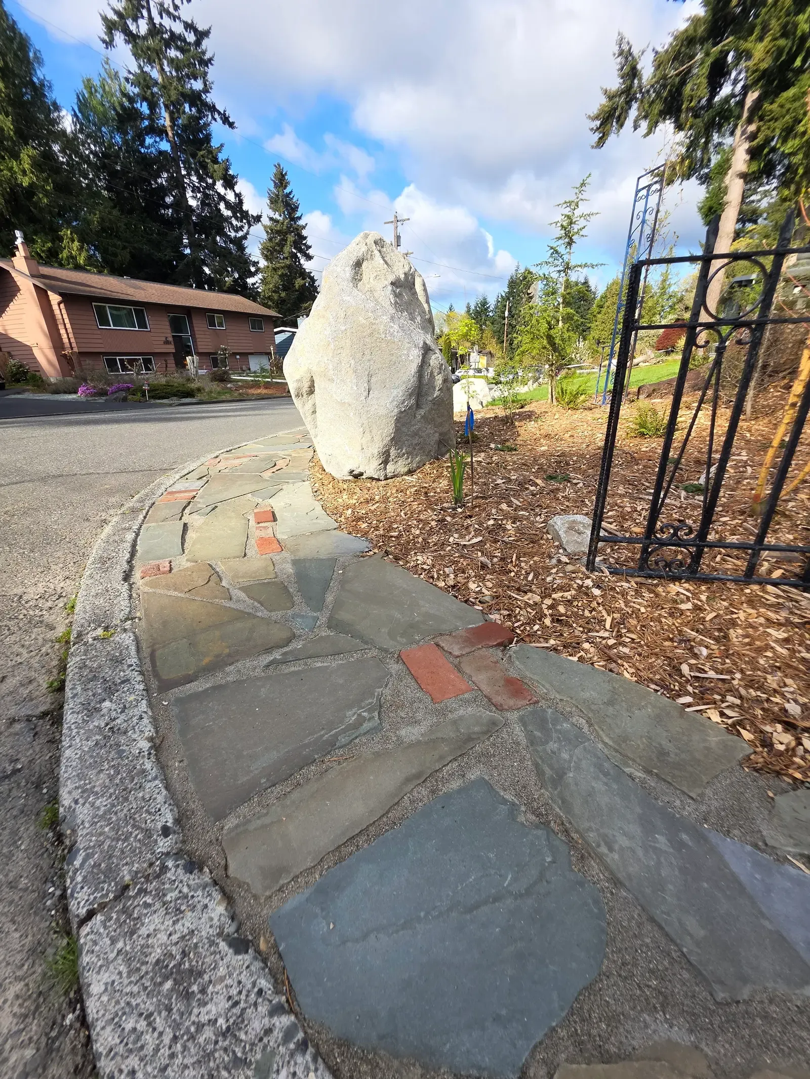 Flagstone path with brick banding running past the boulder under bark mulch