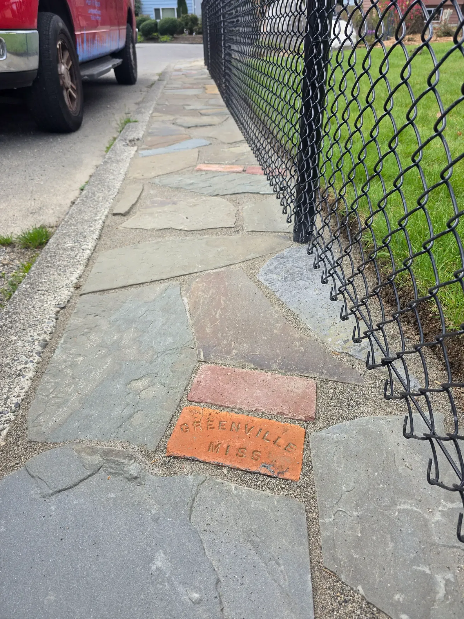Flagstone walk with a stamped brick set into it beside a chain link fence