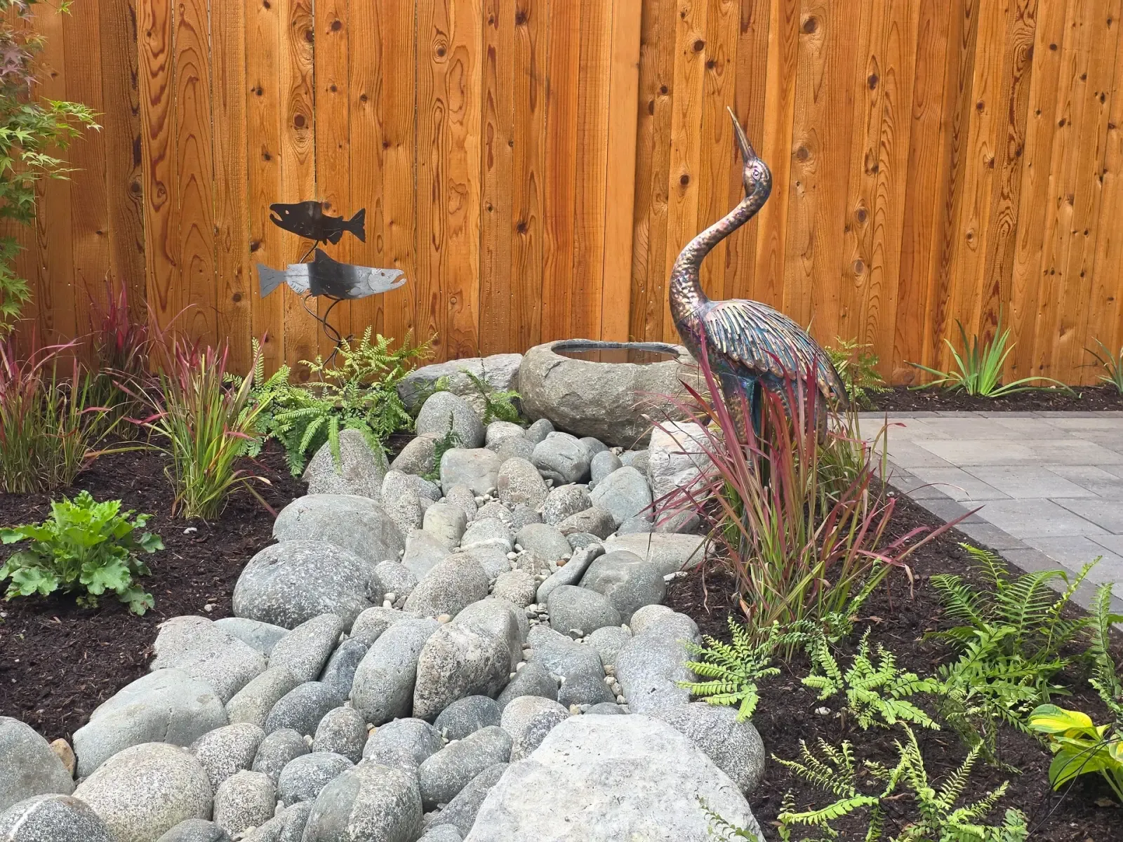 Bronze crane statue and red-toned grasses beside the river cobble and stone dish