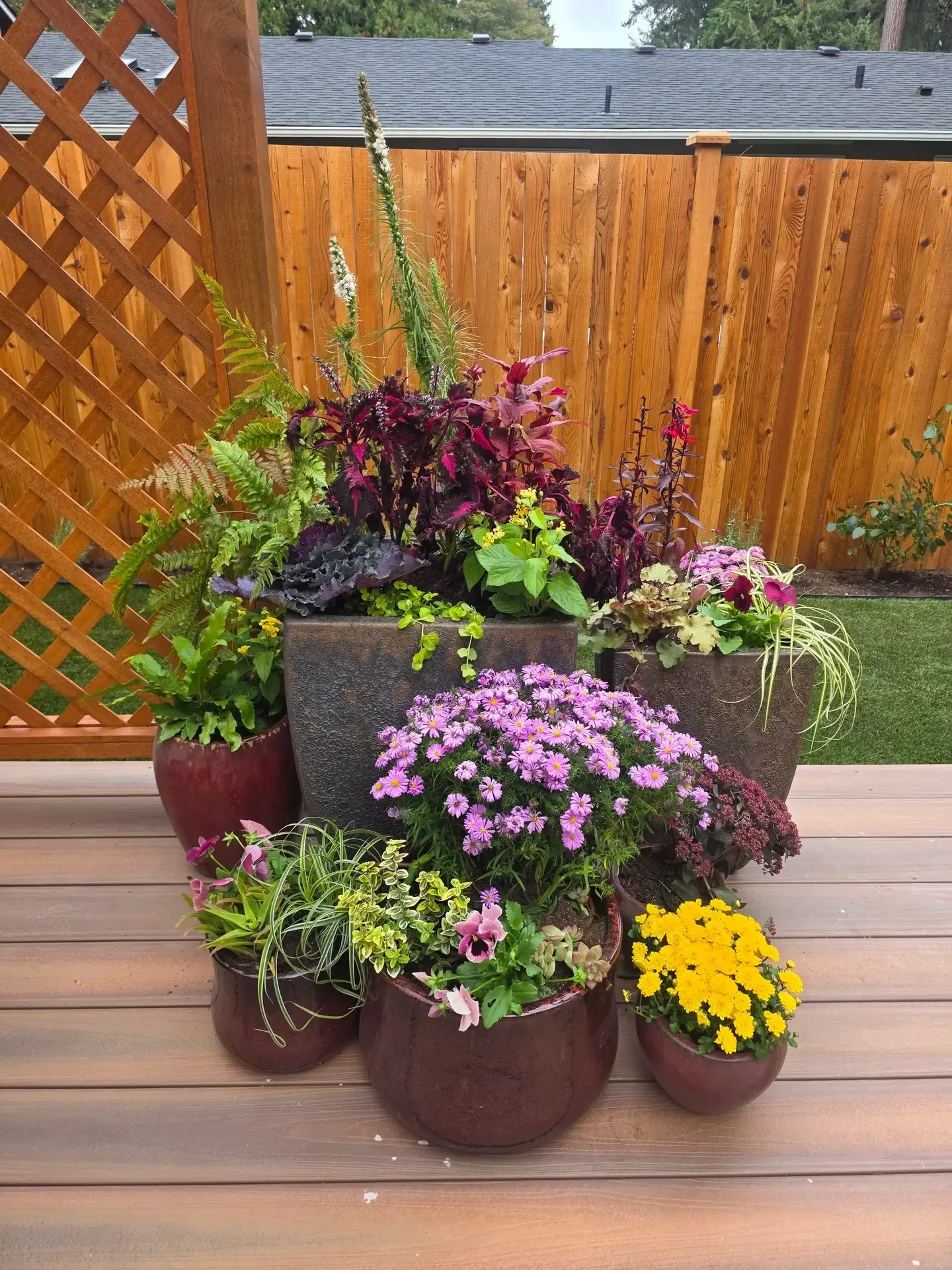 Planted containers grouped on the deck, layered tall to short with seasonal bloomers