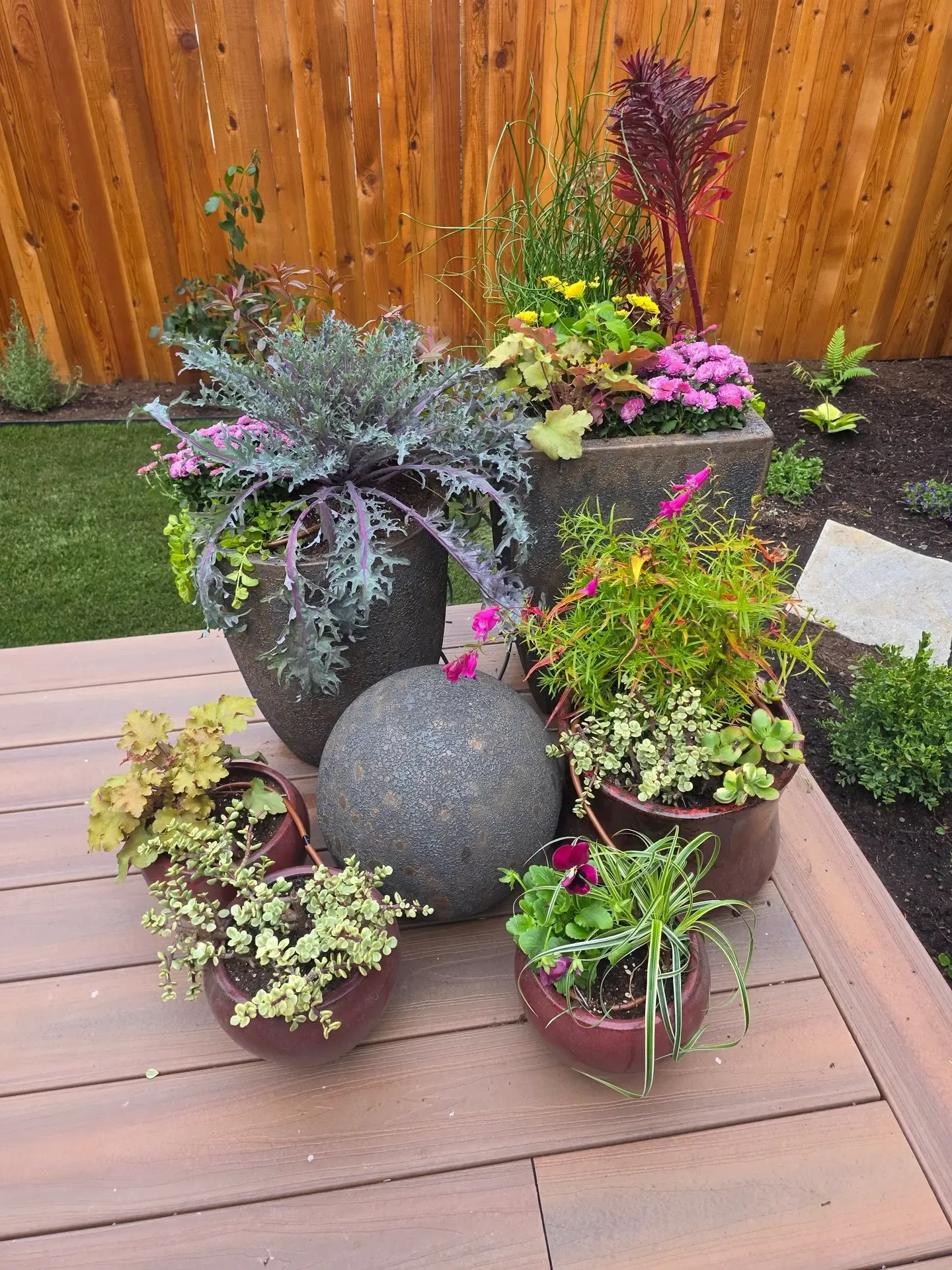 Deck containers with ornamental kale, trailing plants and a concrete sphere accent