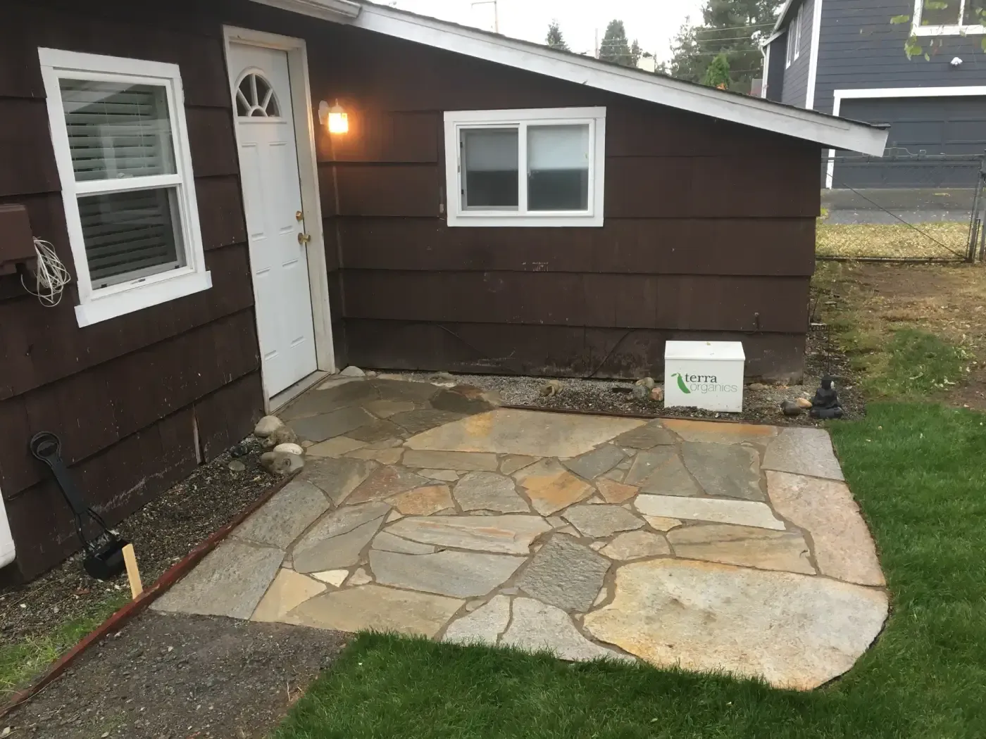Tan flagstone pad at back door of brown house, lawn alongside