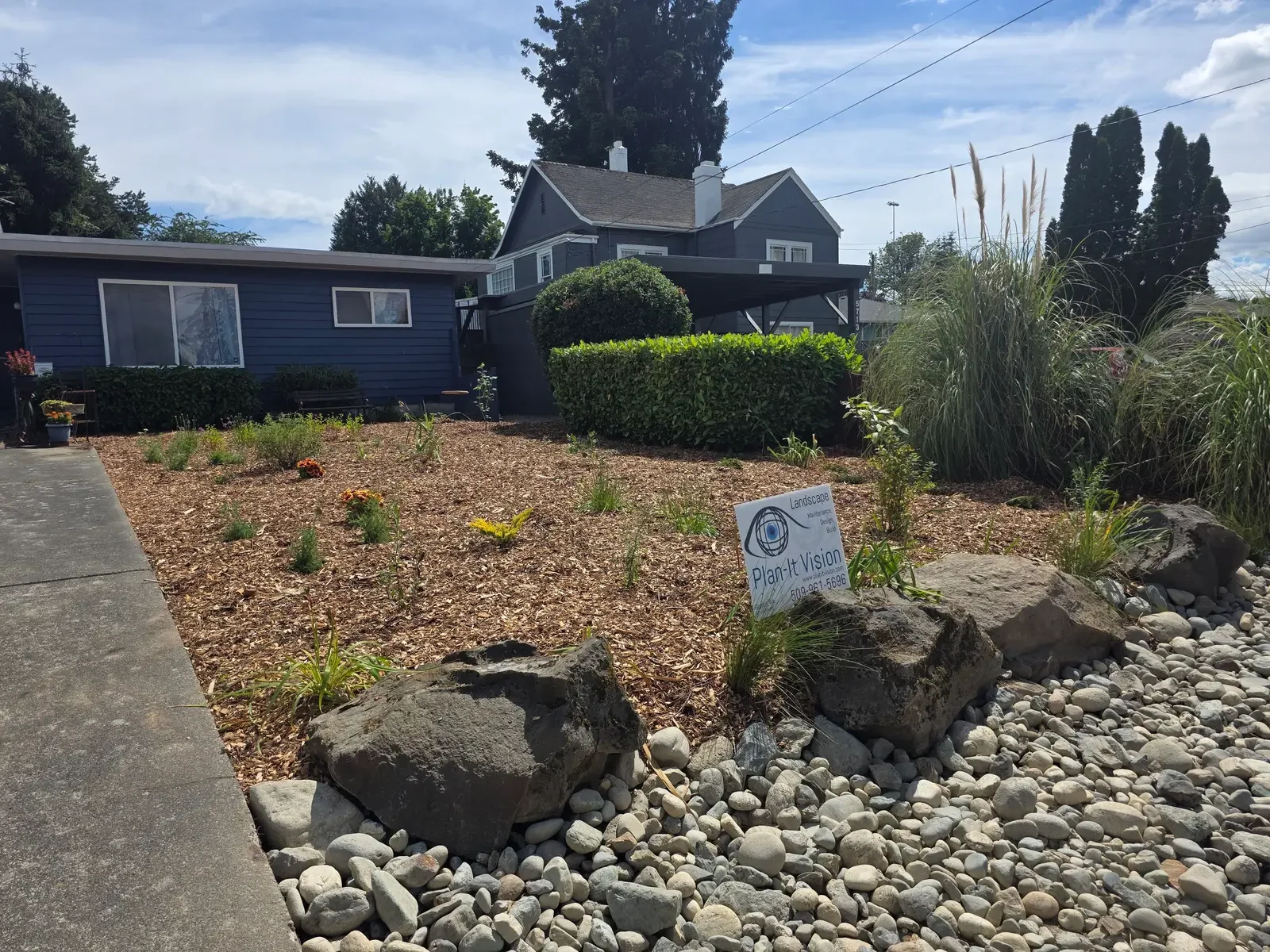 Front garden of native perennials, placed boulders and a river rock dry stream bed