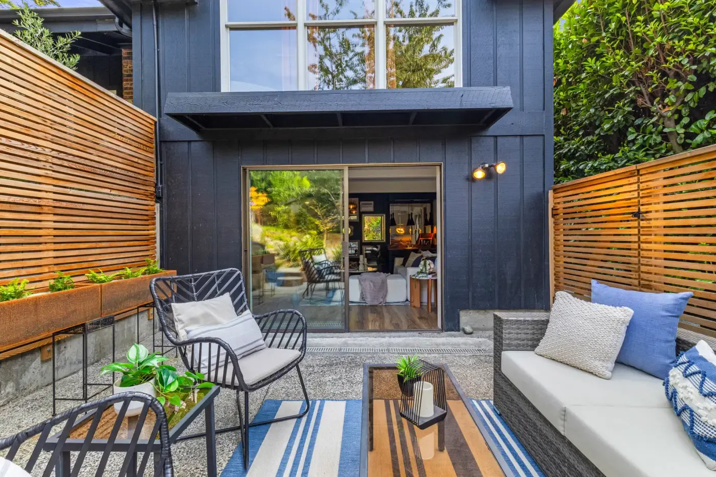 Small courtyard patio enclosed by horizontal cedar slat screens, with steel planter boxes and outdoor seating