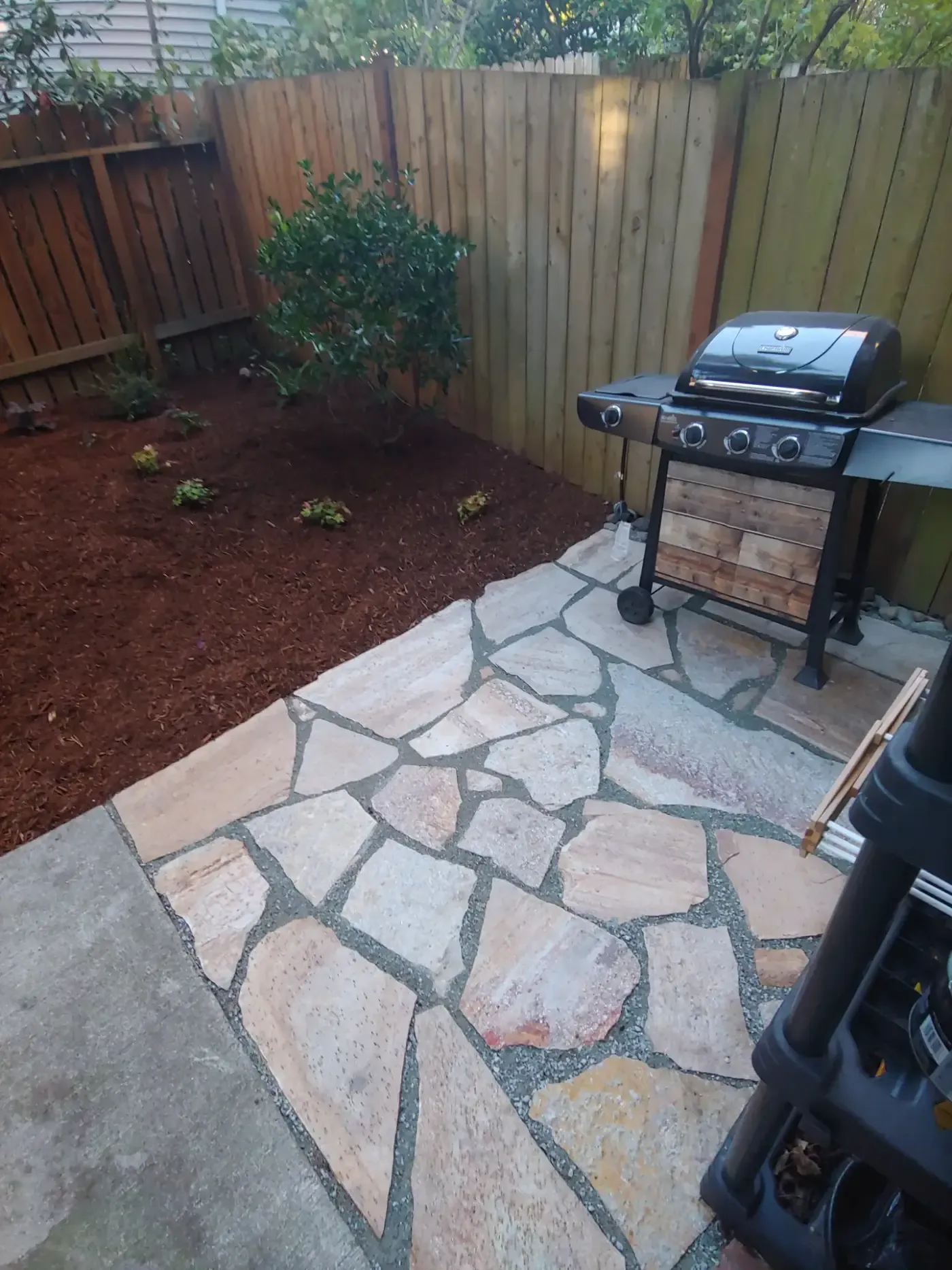 Tan flagstone patio with grill, cedar fence, fresh red mulch bed