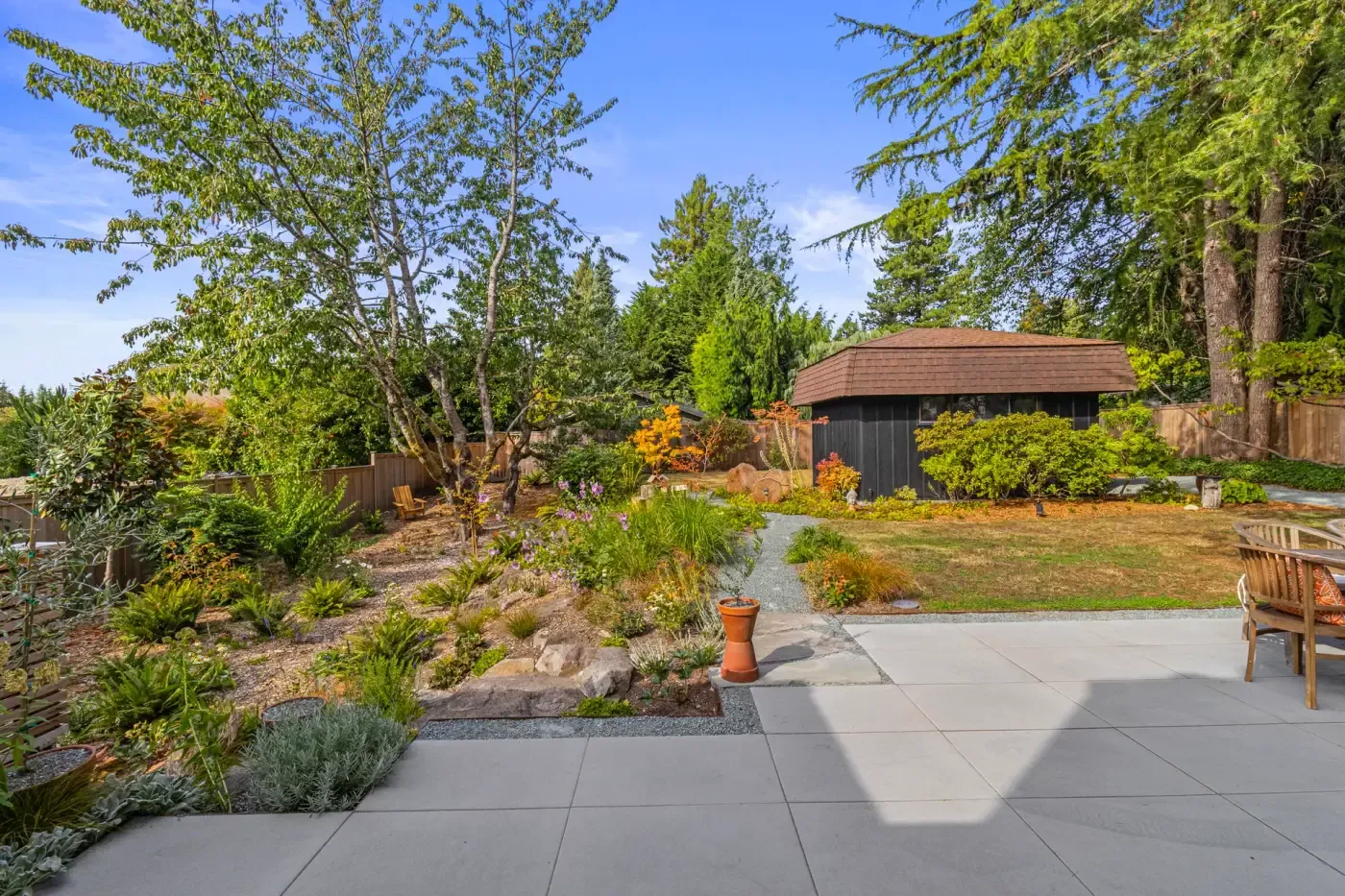 Large format slab patio beside a planted rock garden berm with a gravel path to the garden shed
