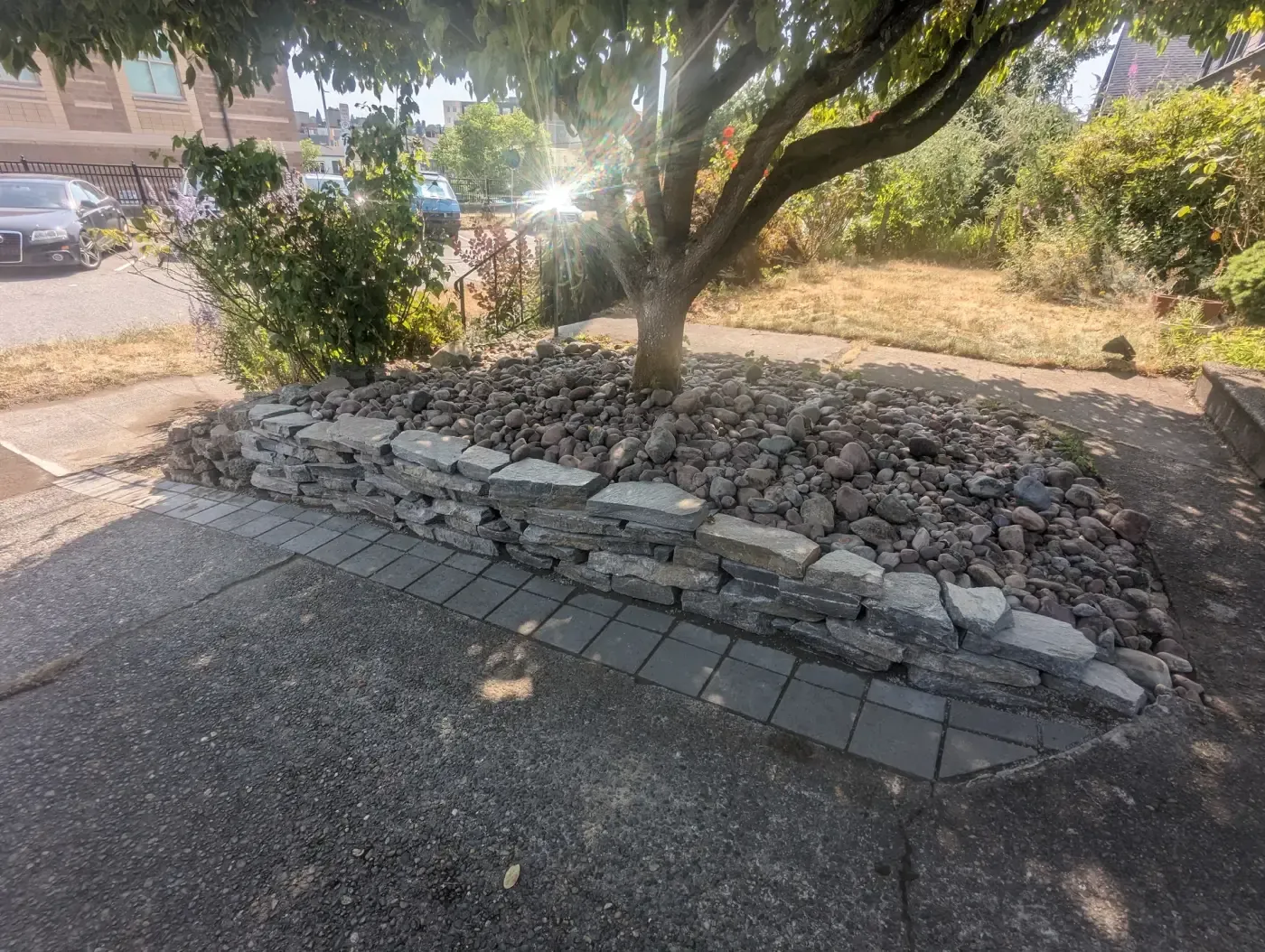 Dry-stacked stone wall retaining river rock bed around street tree