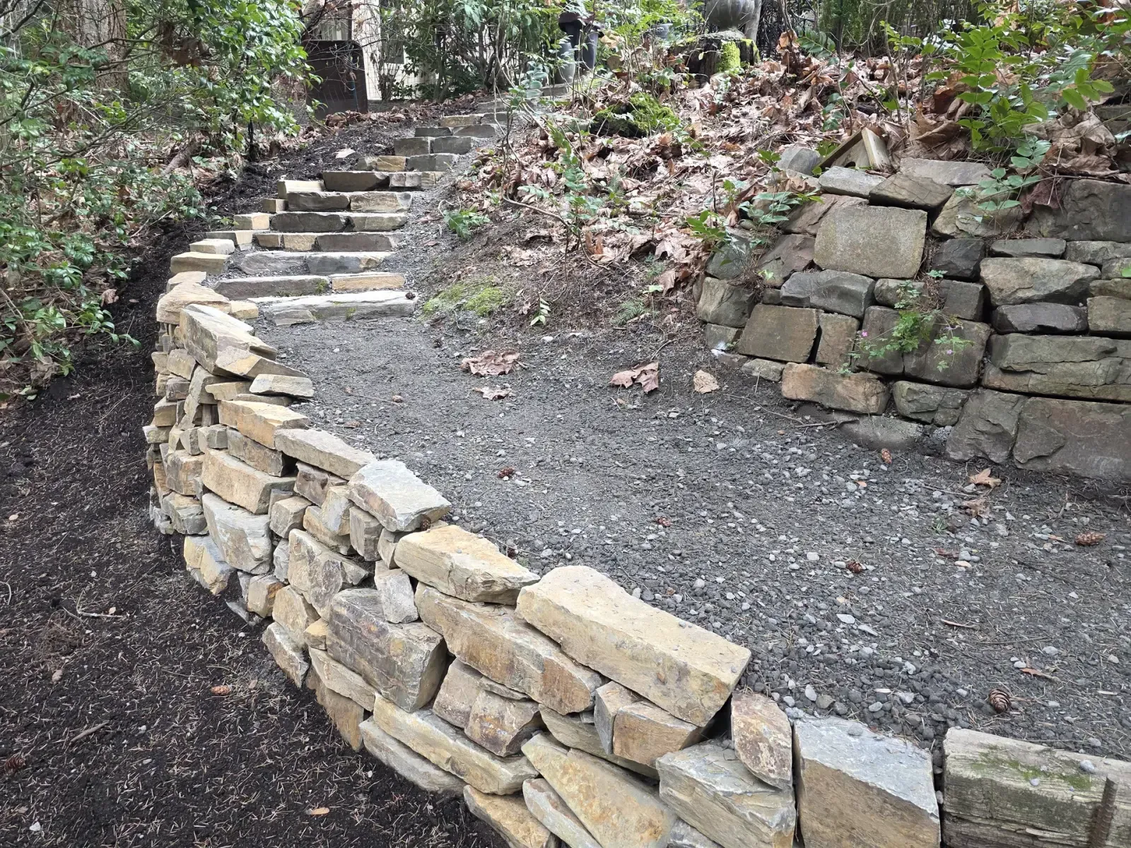Two dry-laid stone walls framing a gravel landing in a wooded setting