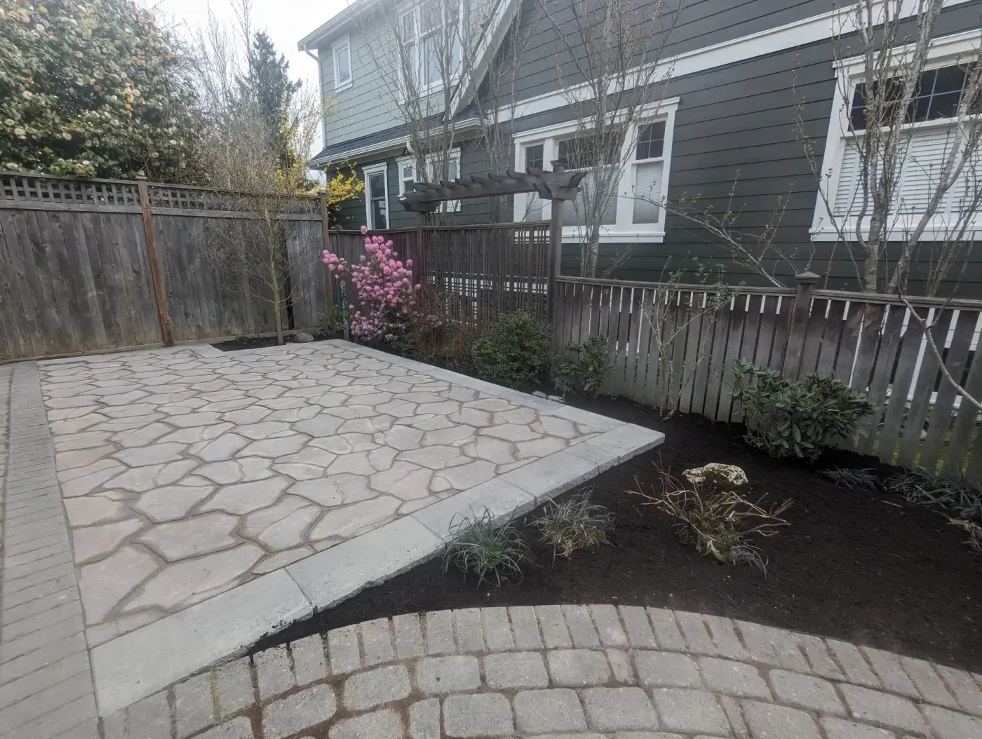 Wide view of a paver terrace with a mulched border and a magnolia
