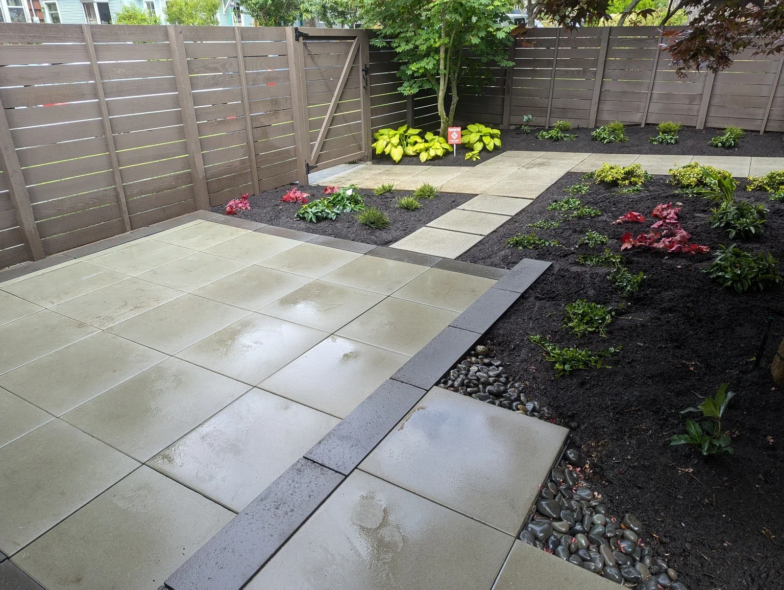 Large format concrete slabs set with dark gravel joints beside freshly planted beds