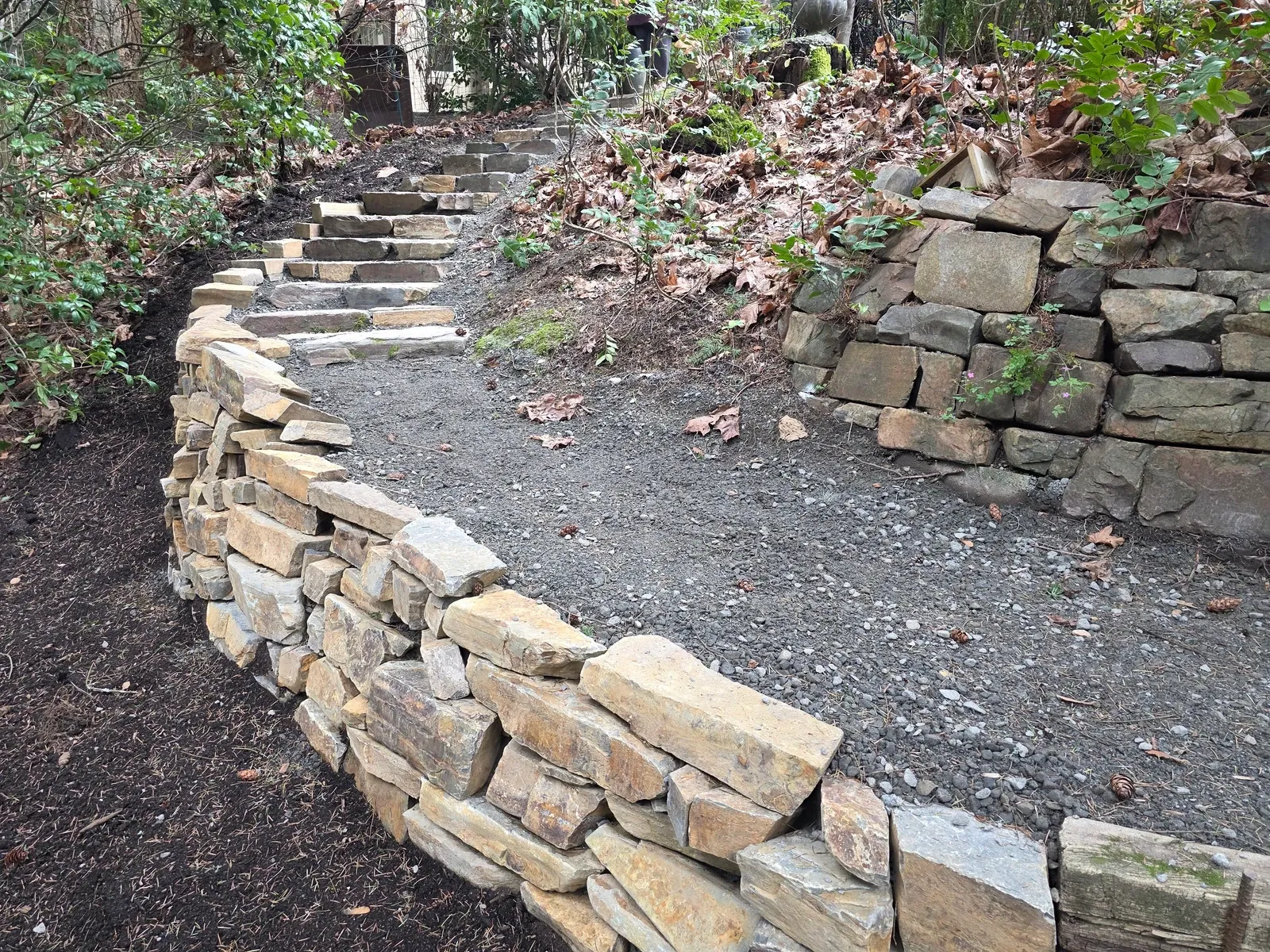 Dry stacked stone retaining wall curving below a run of stone steps on a wooded slope