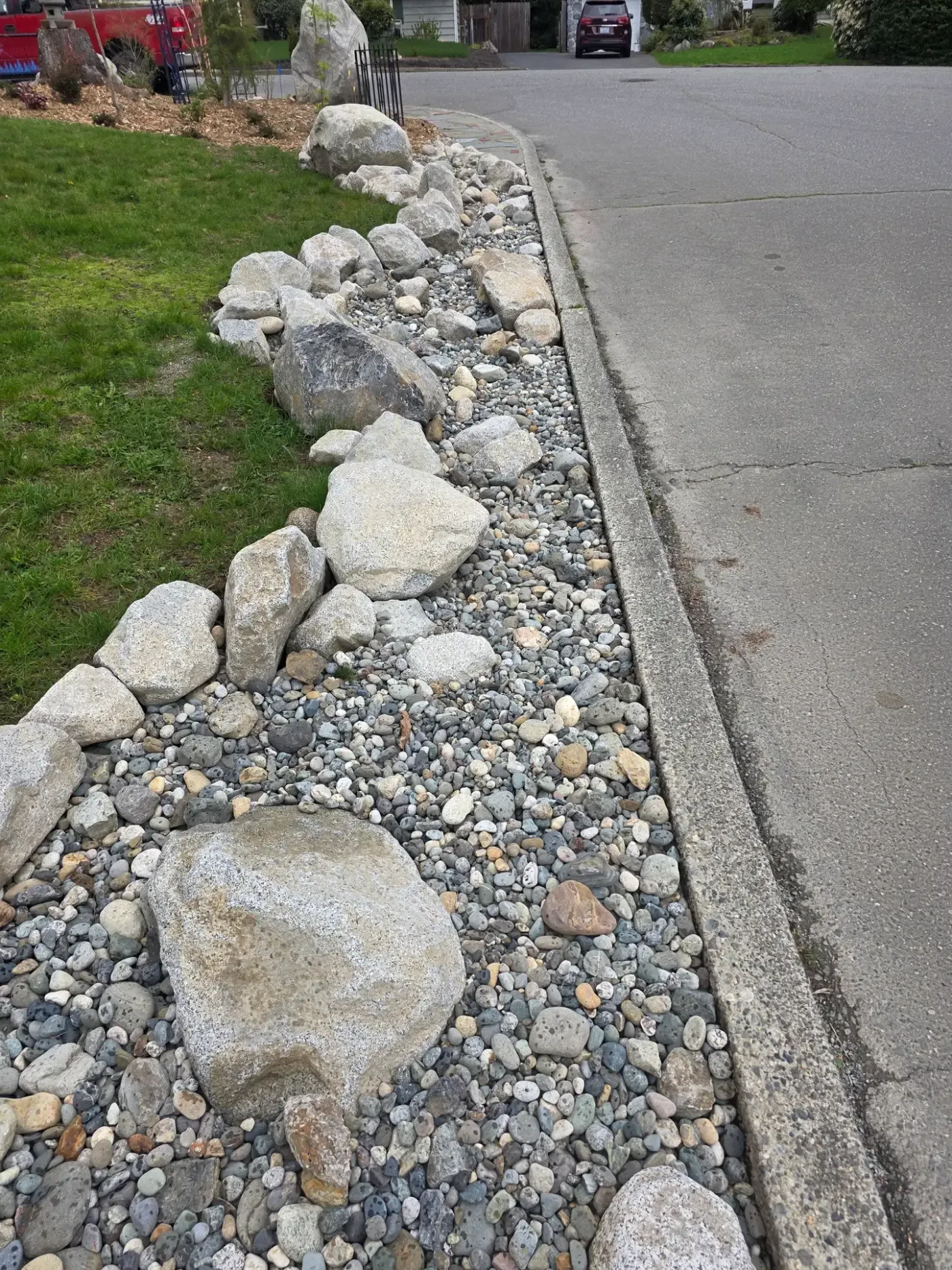 Close view of mixed river rock and set boulders filling a strip along a concrete curb