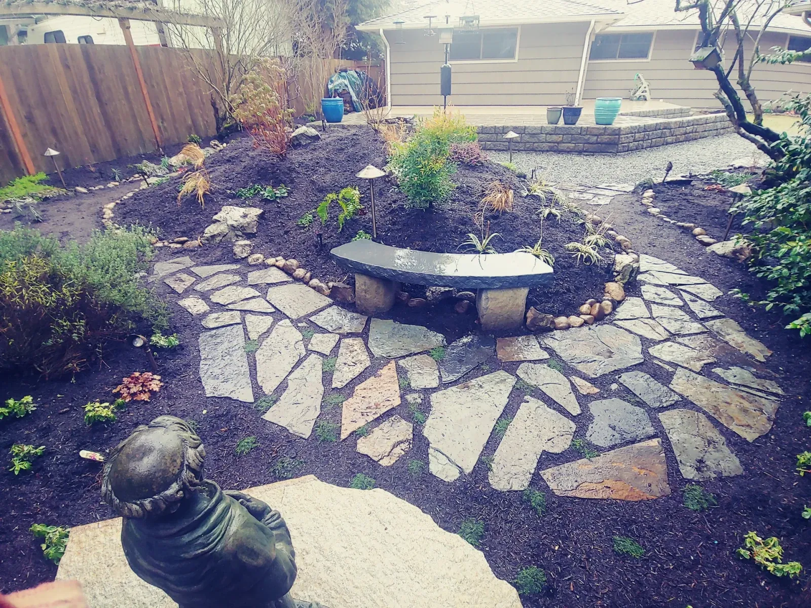 Overhead view of a flagstone courtyard with a mulched berm and a stone bench