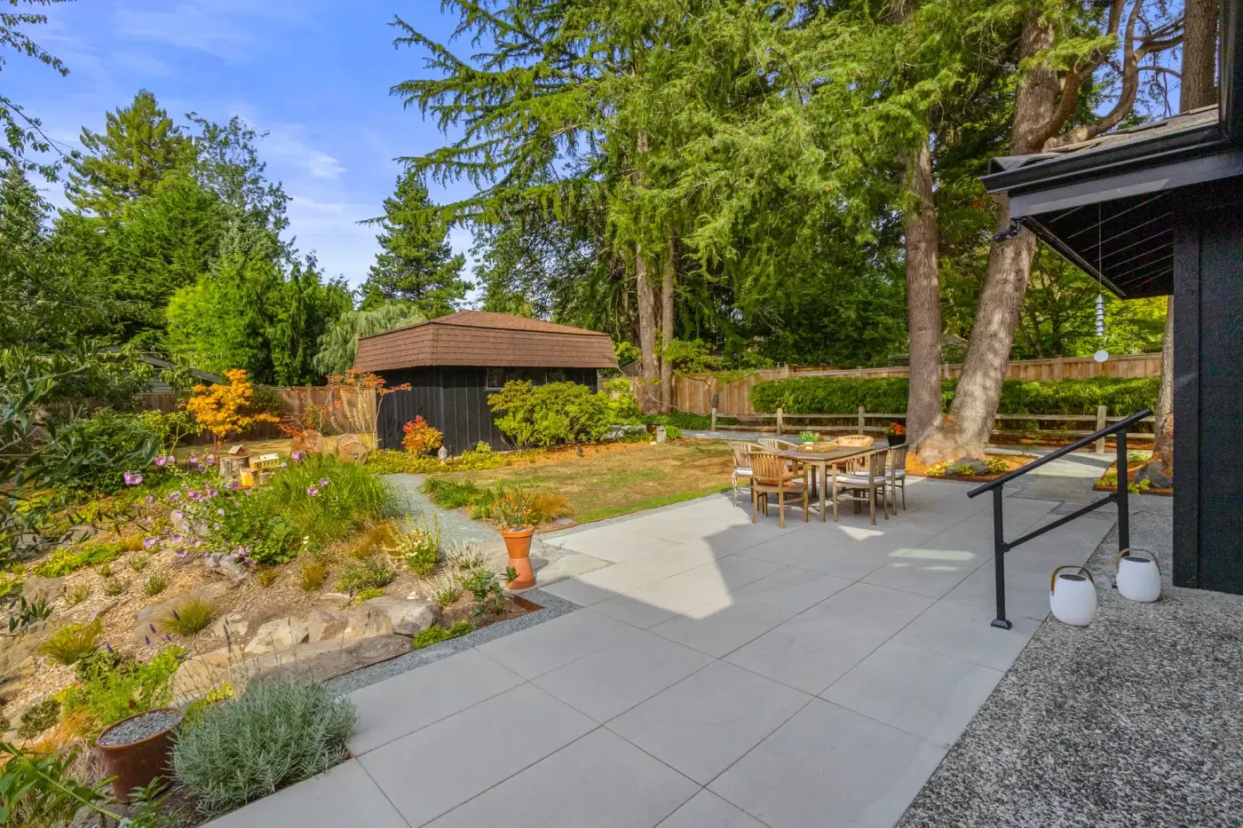Slab patio with a teak dining set, black steel handrail at the back steps and a rock garden alongside