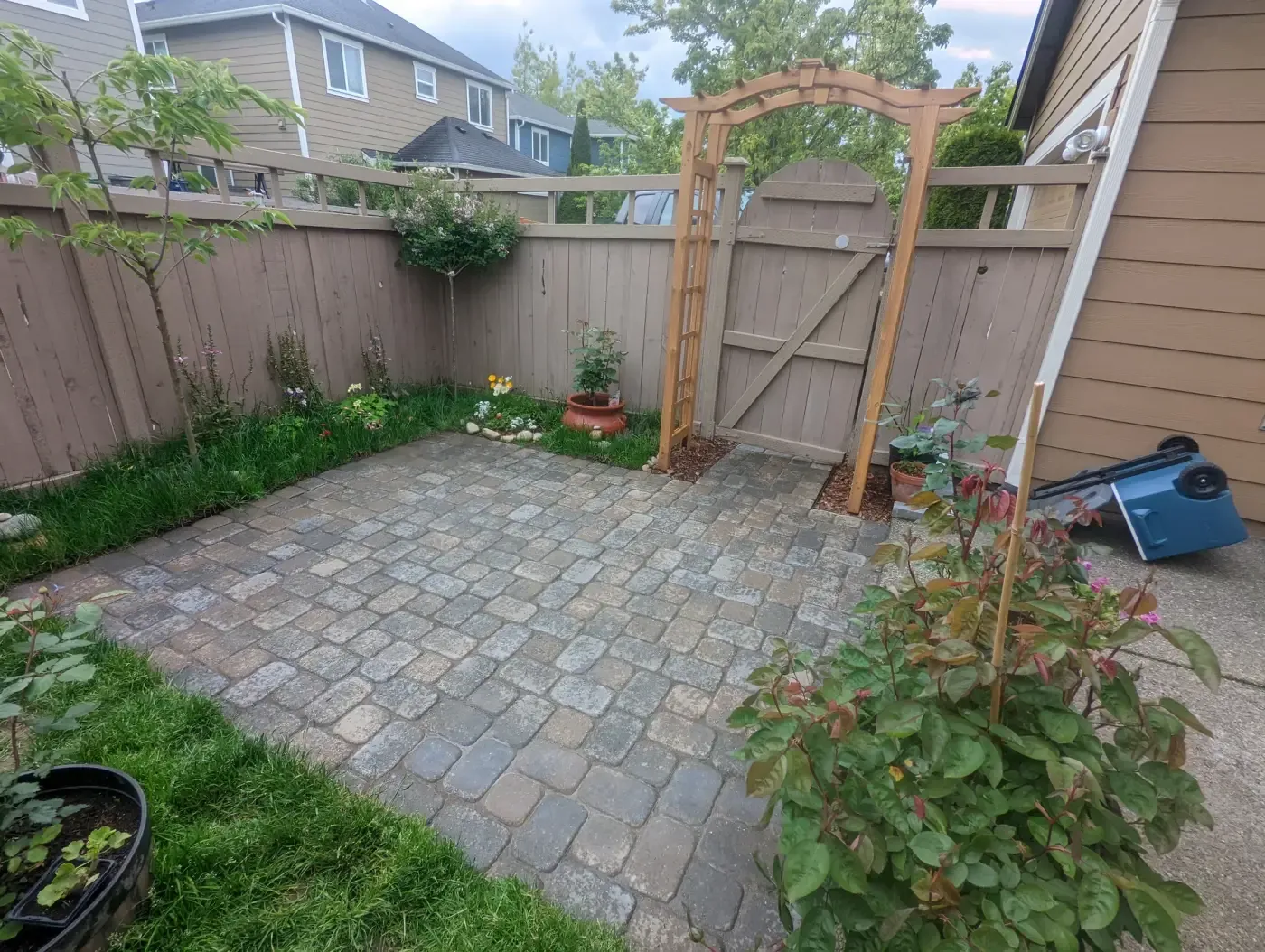 Square tumbled paver patio with cedar arch over side gate