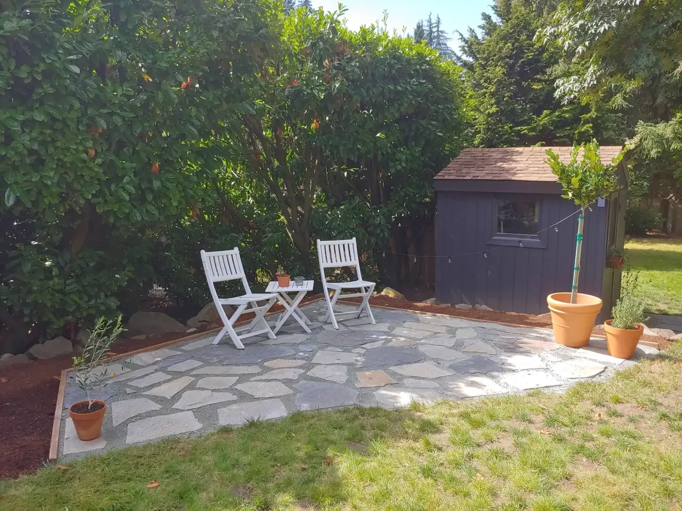 Close view of flagstone terrace, bistro chairs, tall laurel hedge