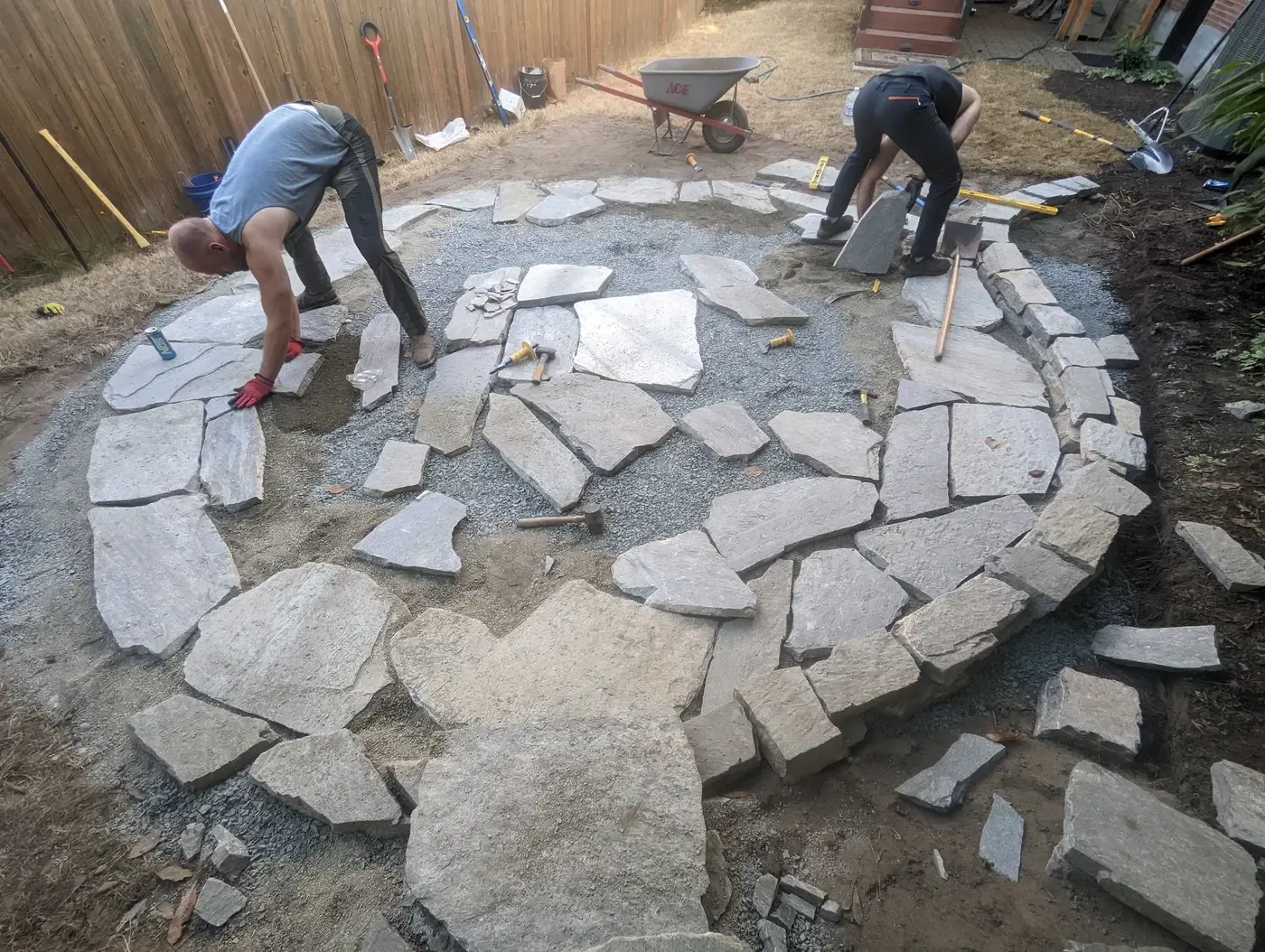 Two crew setting a circular flagstone patio, cut pieces laid out around them