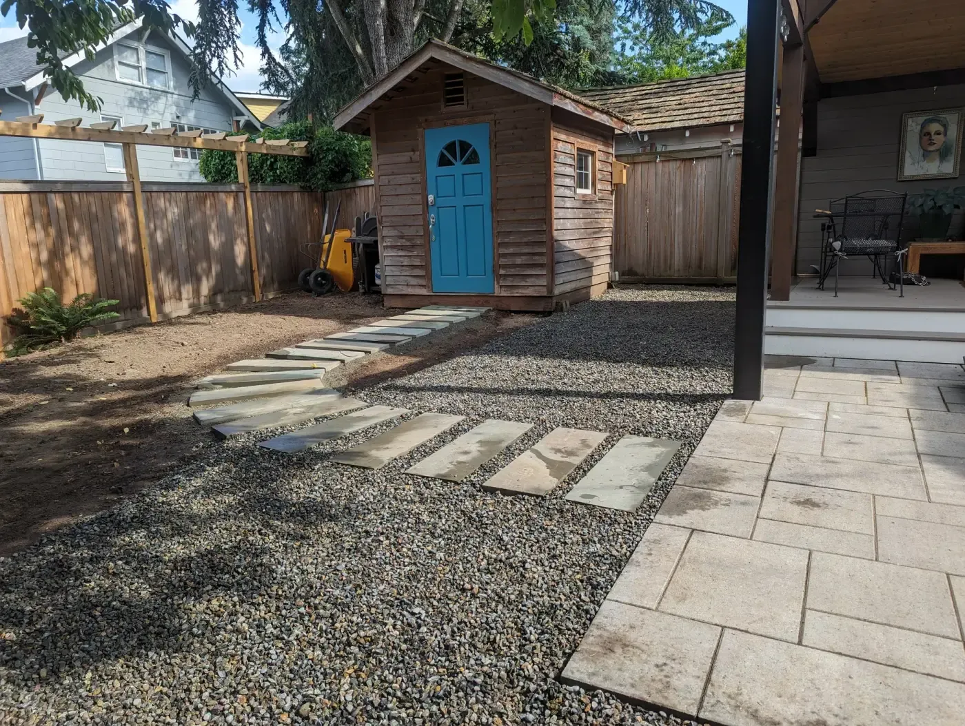 Tan paver patio meets gravel yard with flagstone steppers, shed