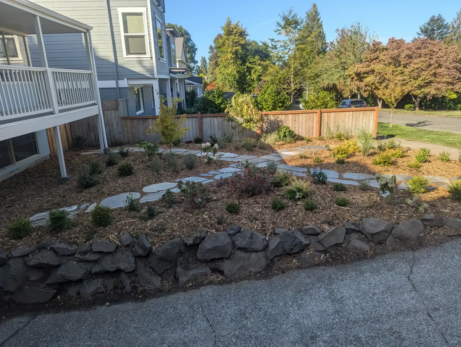 Low boulder wall holding a planted slope above a sidewalk