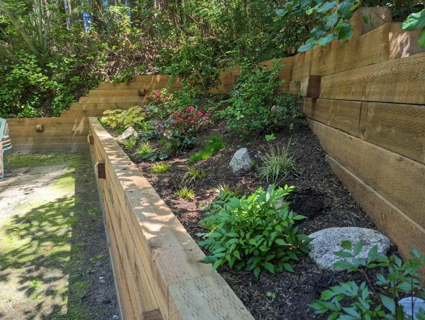 Two-tier timber wall corner with granite boulders and new plants