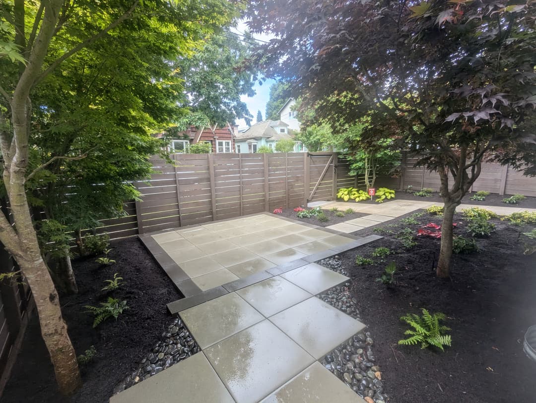 Modern garden design with stone pathway, plants, and wooden fence in a lush green setting.