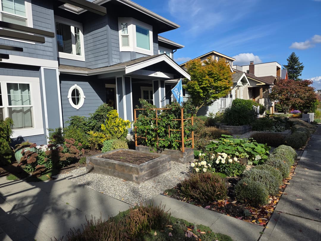 Charming blue house with garden and flag, surrounded by landscaped walkway and trees.