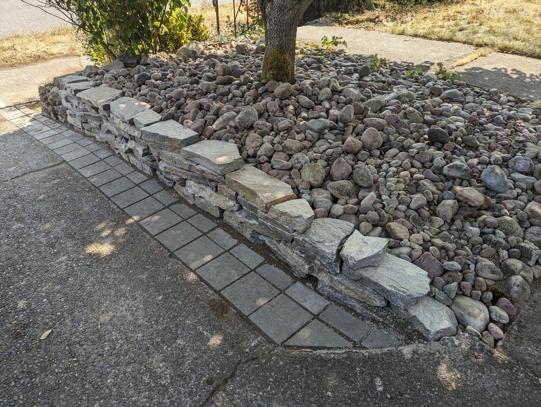 Stone landscaping with a rock garden around a tree and a paved walkway.
